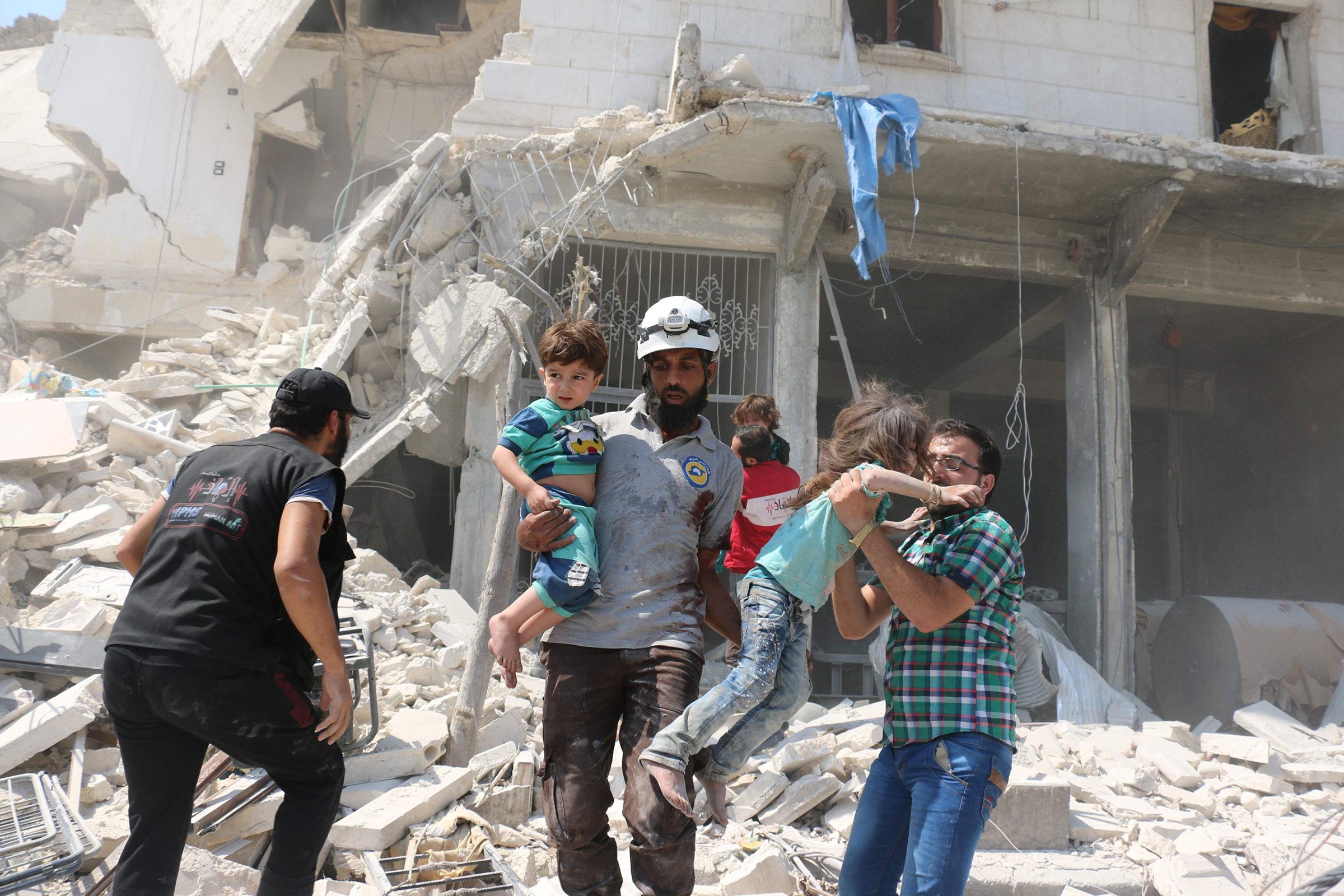 Syrian civilians and a rescue worker evacuate children in the Maadi district of eastern Aleppo after regime aircrafts reportedly dropped explosive-packed barrel bombs on Aug. 27, 2016.