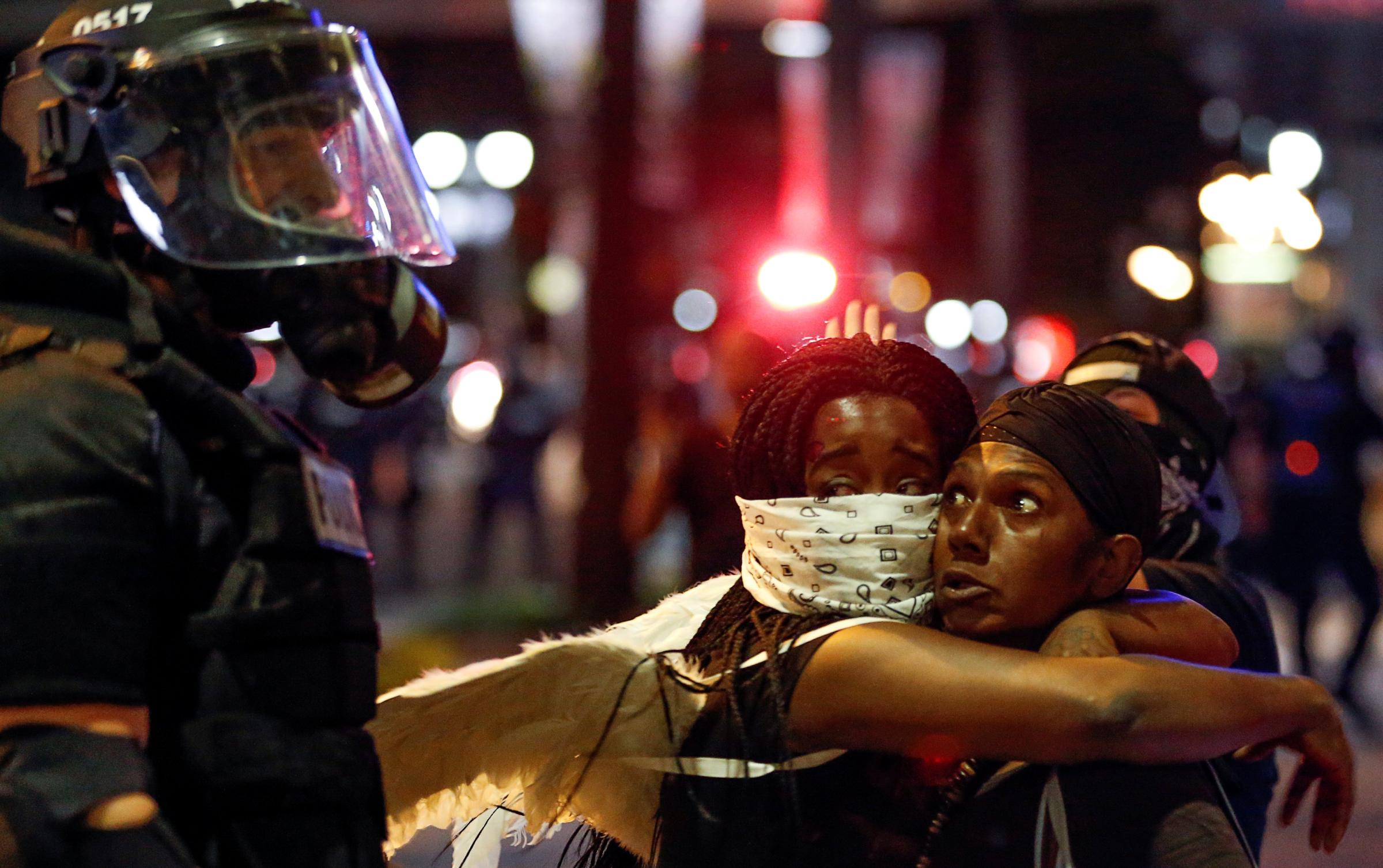 Two women embrace while looking at a police officer in uptown Charlotte, NC during a protest of the police shooting of Keith Scott, in Charlotte