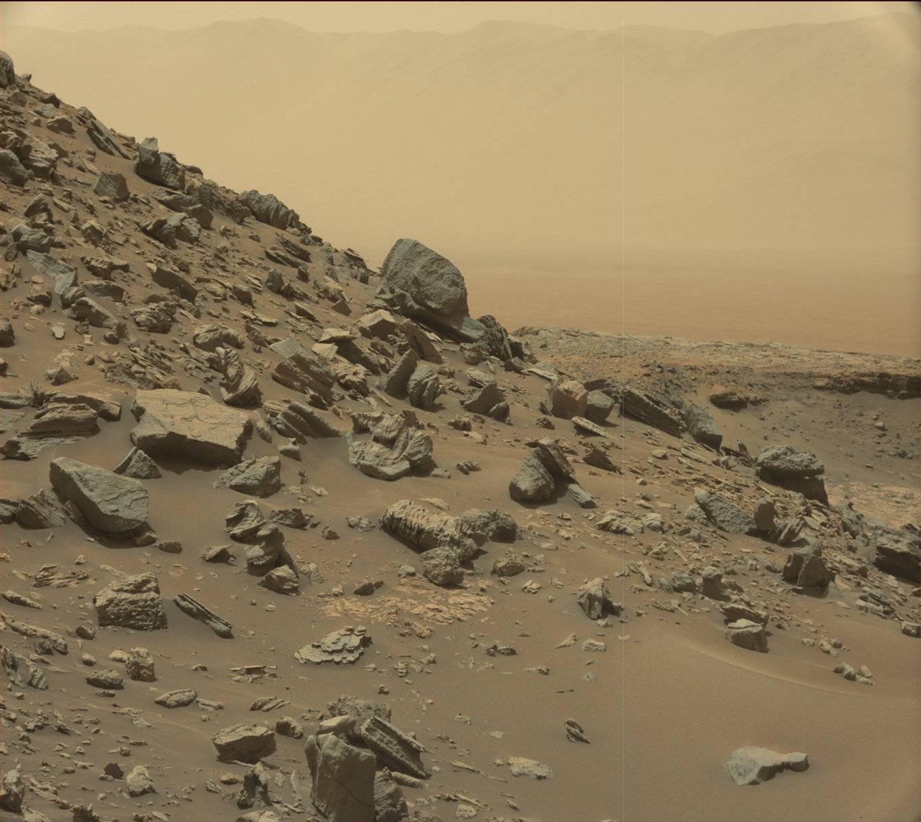 The rim of Gale Crater is visible in the distance, through the dusty haze, in this Curiosity view of a sloping hillside on Mount Sharp.