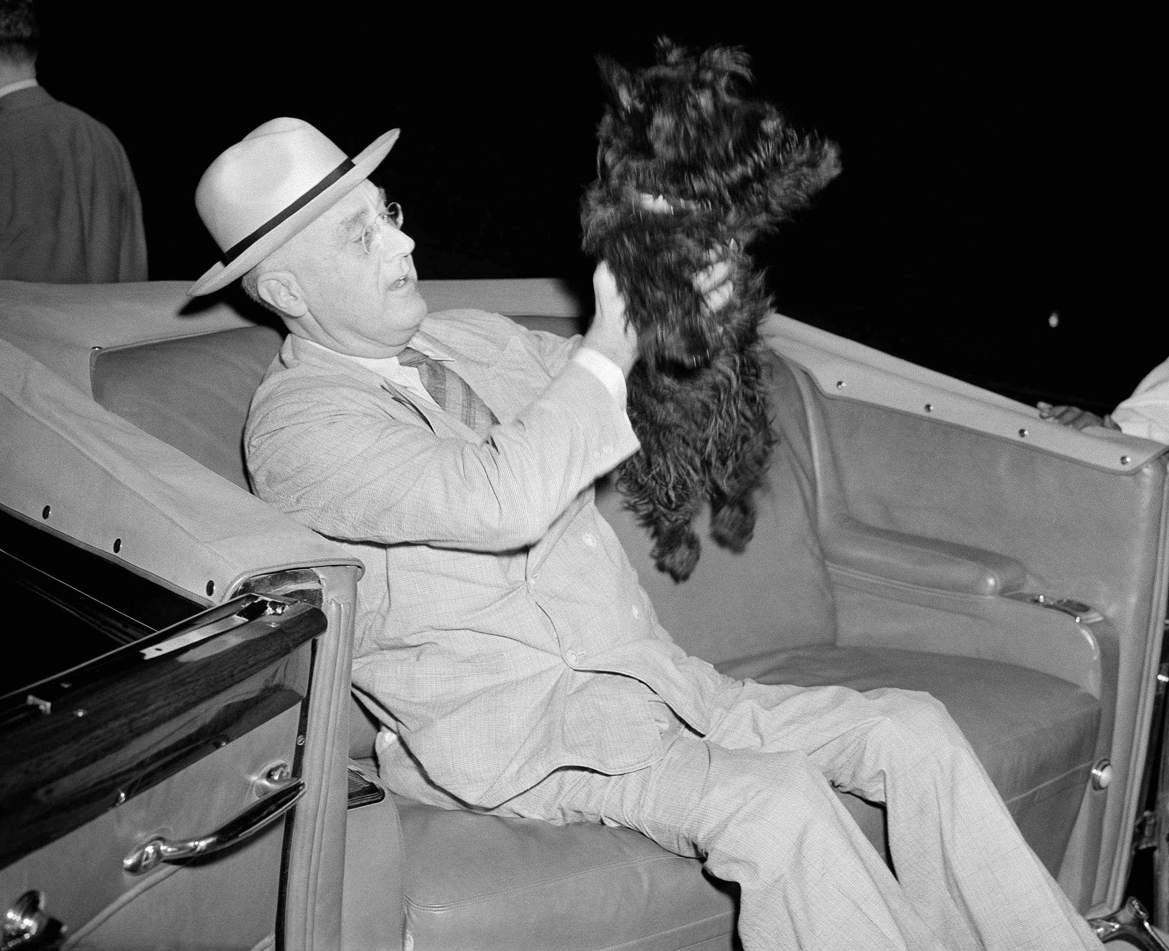 Franklin D. Roosevelt lifts his dog, Fala, as he prepares to motor from his special train to the Yacht Potomac in New London, Connecticut, Aug. 3, 1941.