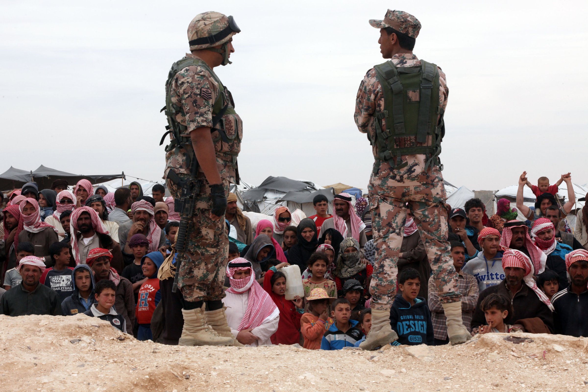 Soldiers stand near Syrian refugees who have arrived at the Jordanian military crossing point of Hadalat at the border with Syria after a long walk through the Syrian desert in Hadalat, Jordan, on May 4, 2016.