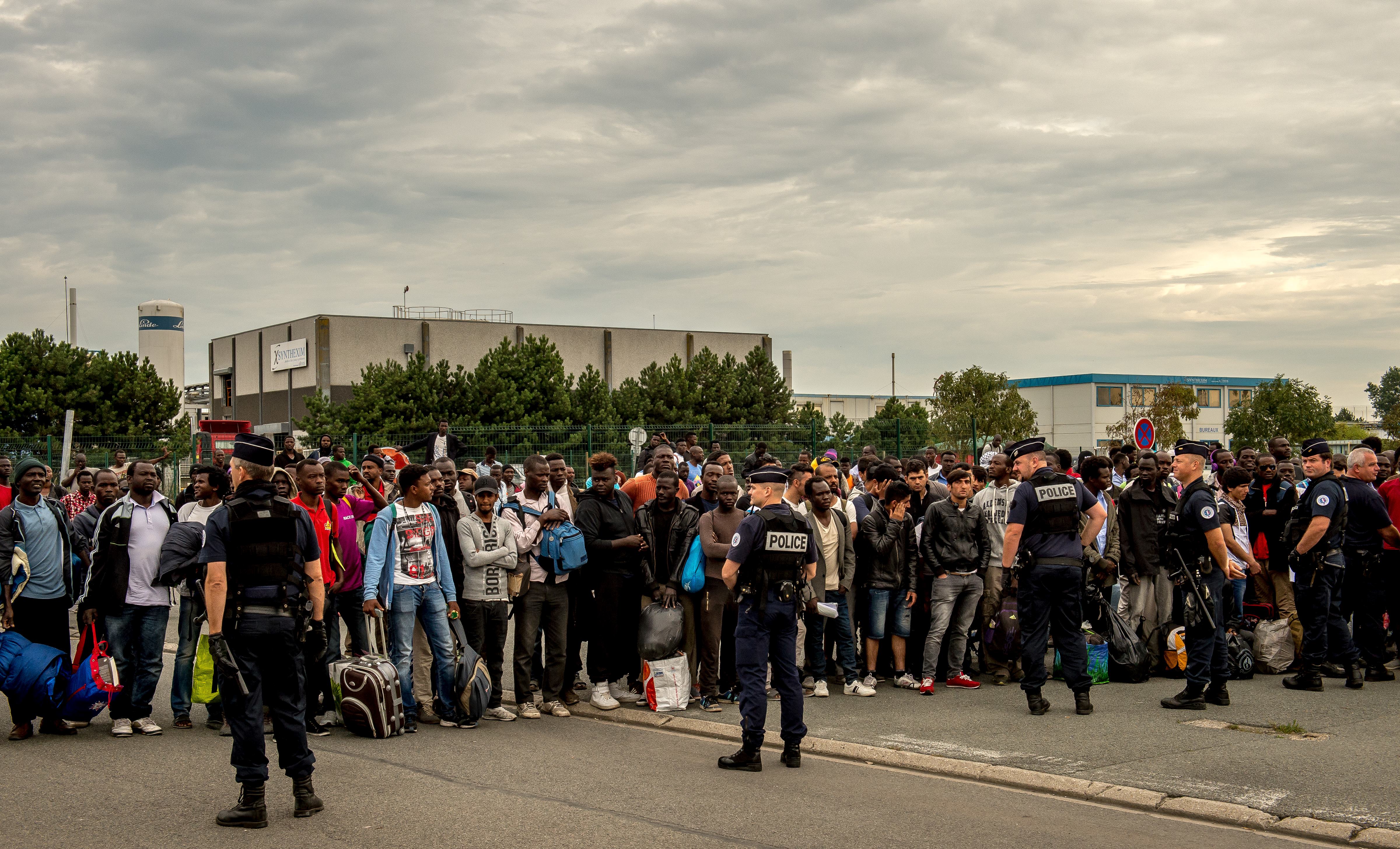 Migrants from the 'Jungle' migrant camp who have been denied access to a bus heading to a "Welcome and orientation centre" (CAO) are gathered under police surveillance, in Calais on Sept. 13, 2016.
