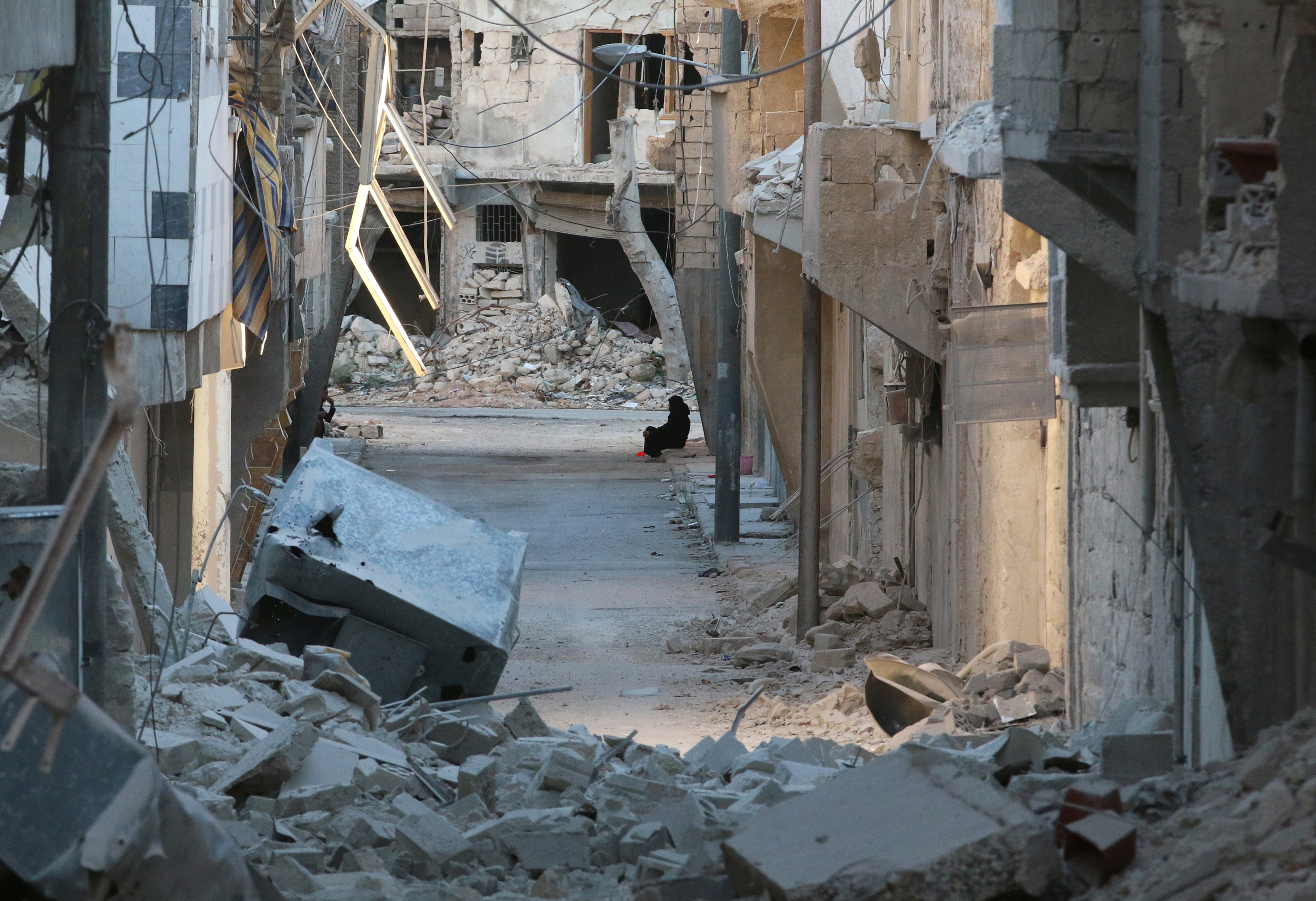 A woman sits amid damaged buildings in the rebel-held al-Myassar neighbourhood of Aleppo