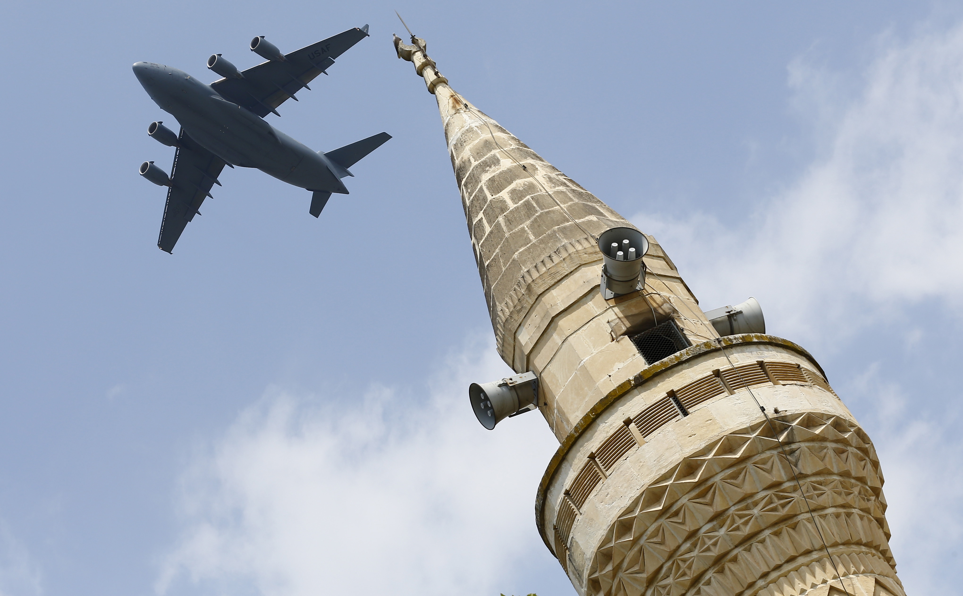 A U.S. Air Force Boeing C-17A Globemaster III large transport aircraft flies over a minaret after taking off from Incirlik air base in Adana