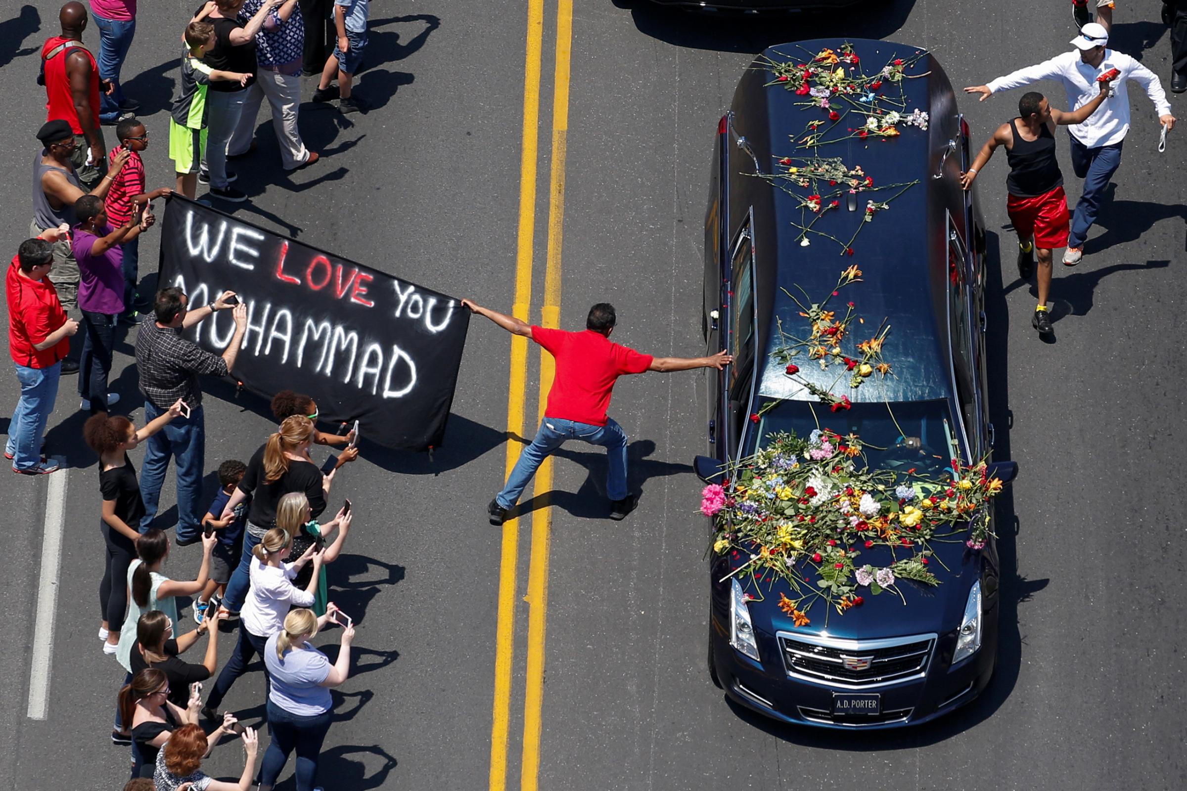 A banner stating "We Love You Muhammad" is displayed as well-wishers touch the hearse carrying the body of the late boxing champion Muhammad Ali during his funeral procession through Louisville, Kentucky, June 10, 2016.
