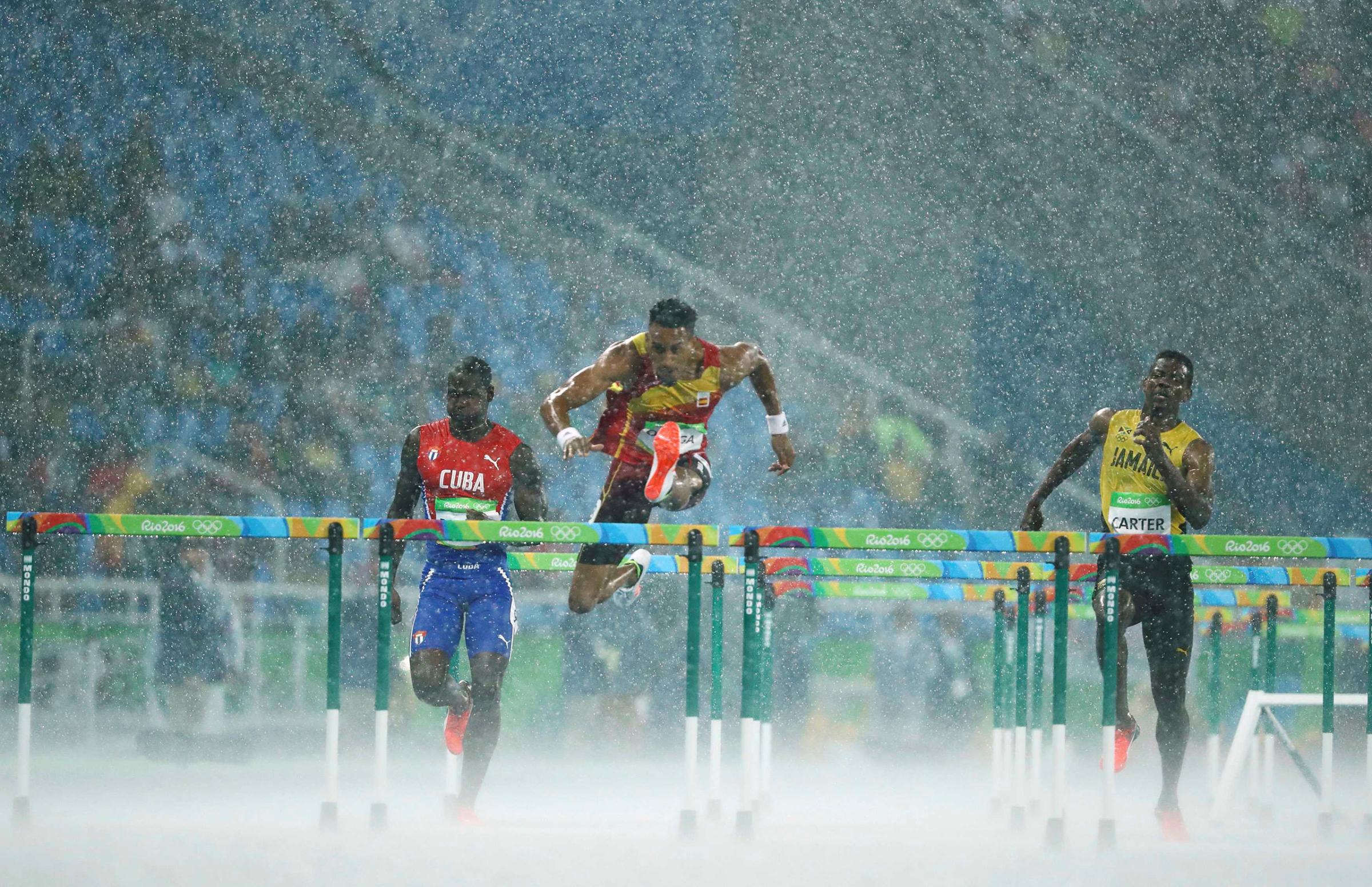 Jhoanis Portilla of Cuba, Orlando Ortega of Spain and Deuce Carter of Jamaica compete in the rain during the 2016 Rio Olympics Men's 110m Hurdles in Rio de Janeiro, Brazil, Aug. 15, 2016.