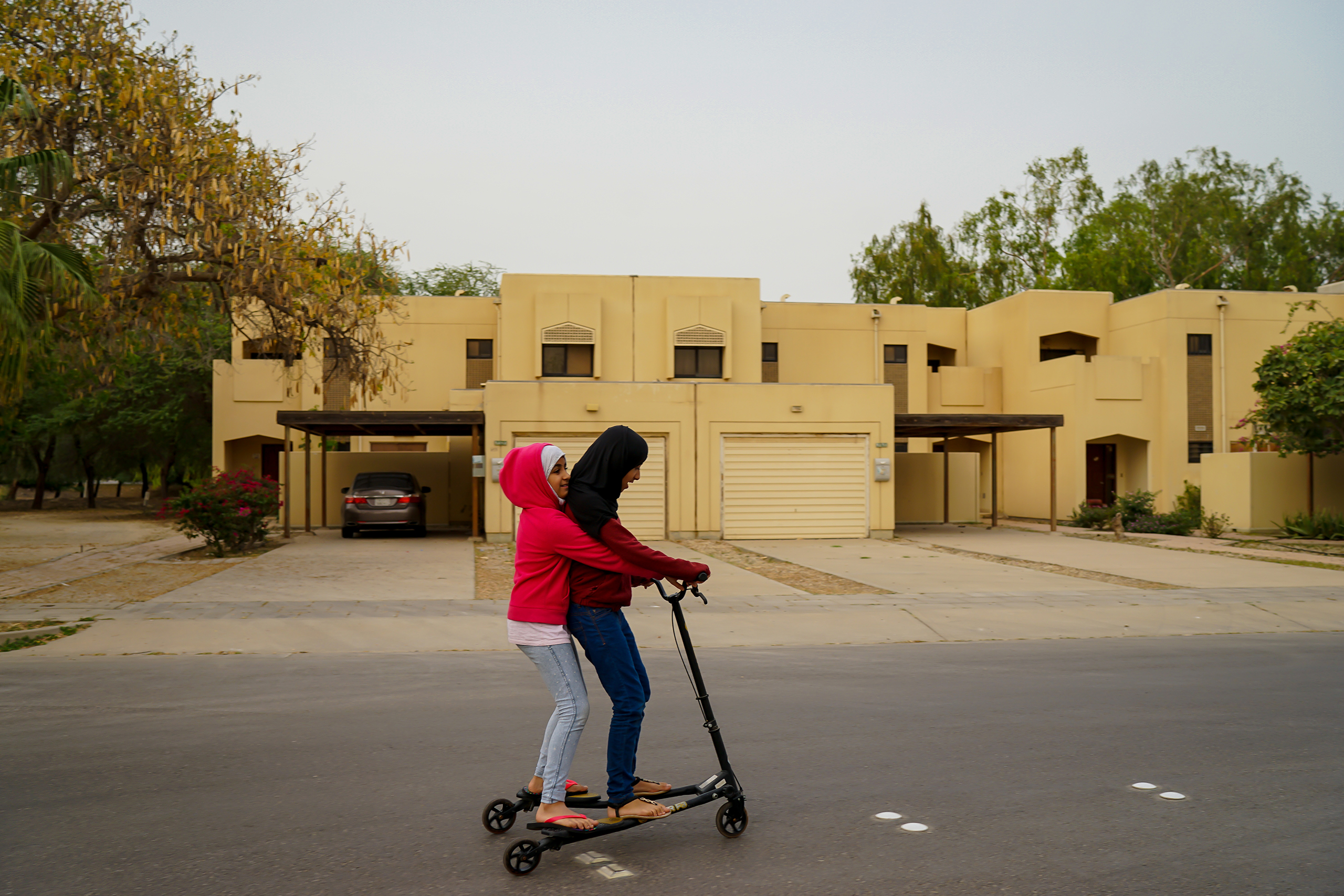 The photographer's daughters, Sura and Yara, ride a scooter around the block of their neighborhood in Jubail Industrial City, April 2016. As they appear young, Alsultan says, no one will harass them.