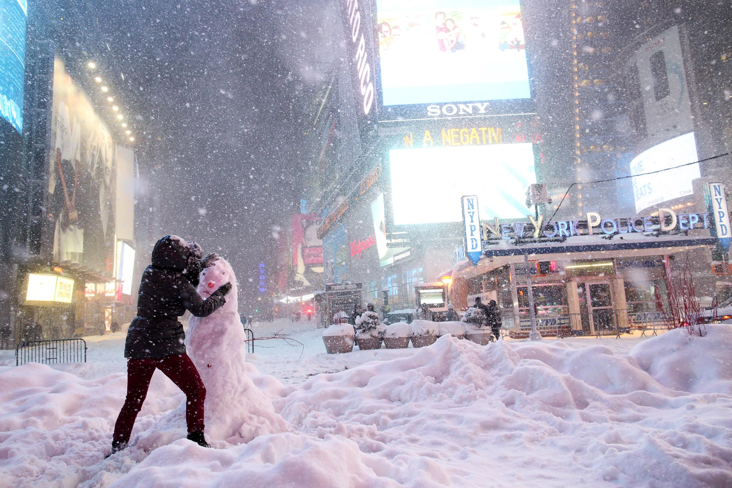 A woman decorates a snowman in Times Square as all cars but emergency vehicles are banned from driving on the road in New York City on Jan. 23, 2016.