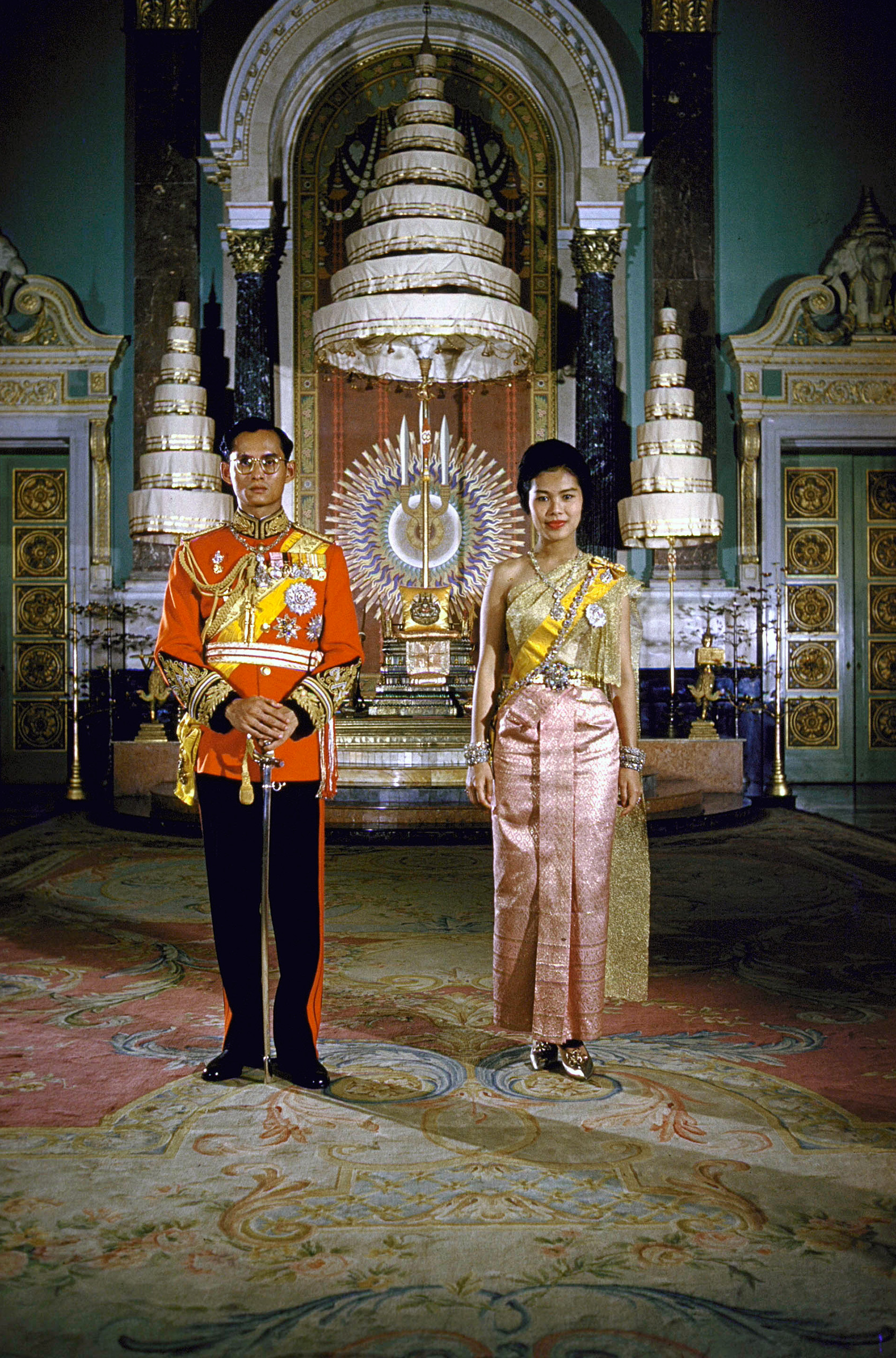 Formal portrait of Thailand's King Bhumibol Adulyadej (aka Phumiphon Aduldet) and Queen Sirikit at the Palace in 1960. The nine-tiered parasol in background is a symbol of the Chakri Dynasty.