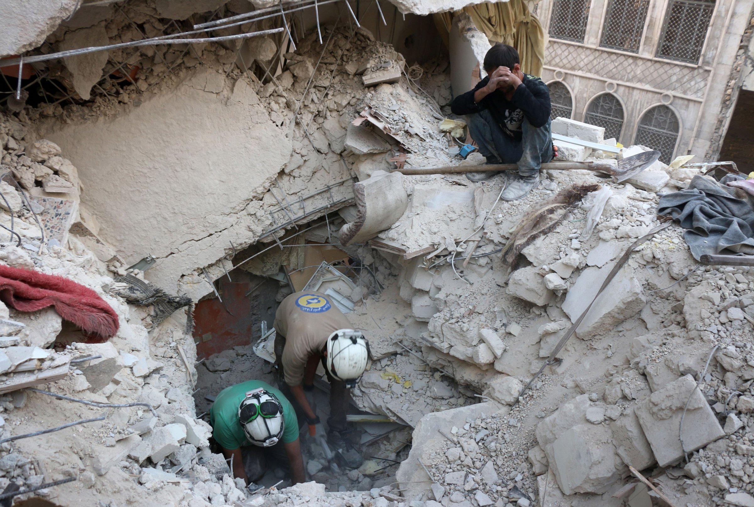 TOPSHOT - Syrian civil defence volunteers, known as the White Helmets, search for victims amid the rubble of destroyed buildings following a government forces air strike on the rebel-held neighbourhood of Bustan al-Basha in the northern city of Aleppo, on October 4, 2016. Assad's forces advanced on rebels during intense street fighting in the opposition-held east of Aleppo city, which Russia has been accused of bombing indiscriminately including targeting its hospitals. / AFP / THAER MOHAMMED (Photo credit should read THAER MOHAMMED/AFP/Getty Images)