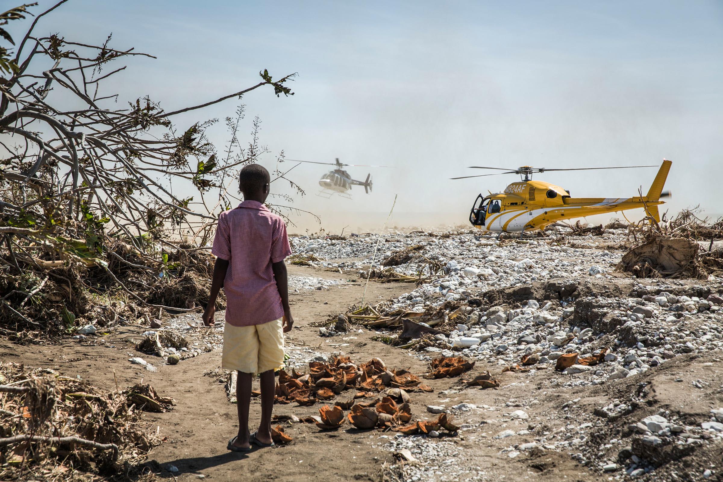 A young boy watches helicopters carrying politicians to the worst hit areas land in Roche-a-Bateau, southwestern Haiti, on Oct. 8, 2016.