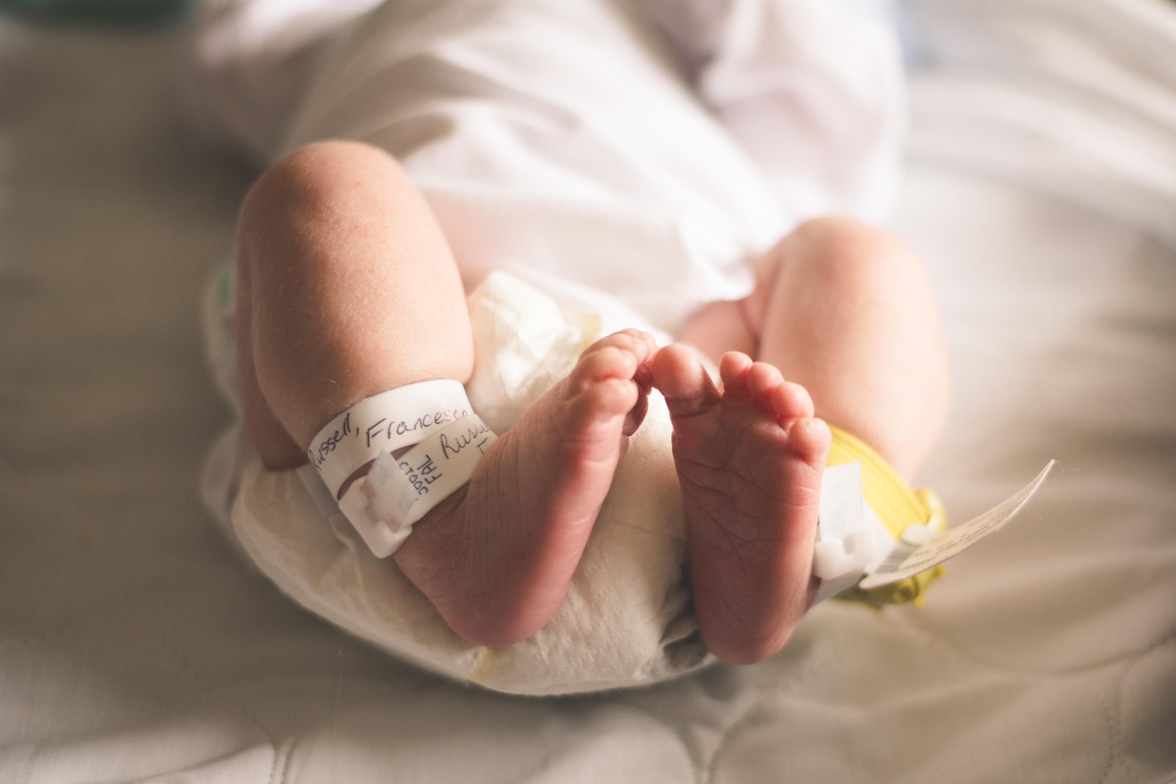 Newborn baby with tiny feet and name bracelets laying on bed in hospital