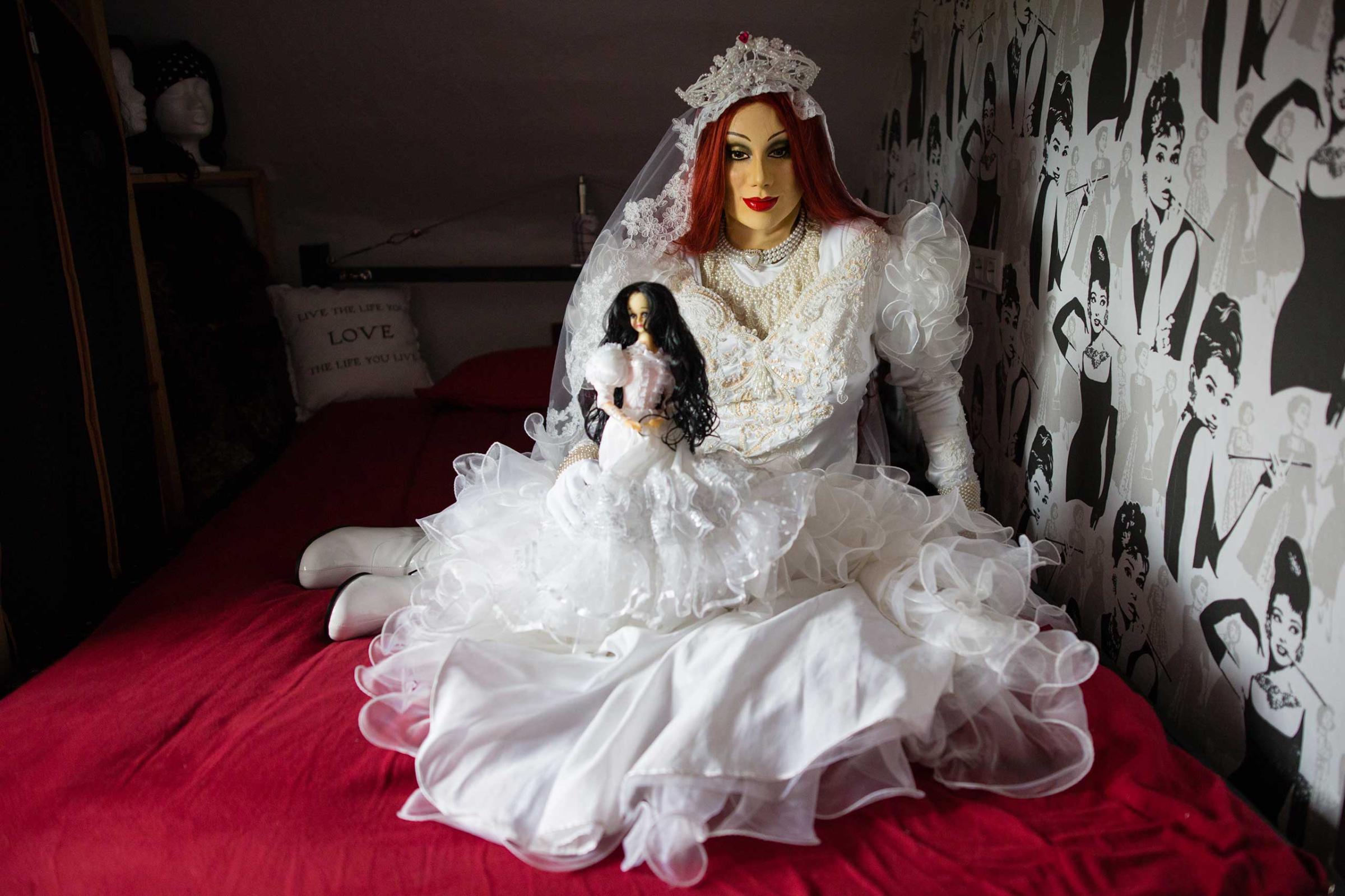 BRAUNSCHWEIG, GERMANY - JUNE 20, 2016: Portrait of female masker Andre, 30, alias 'Lisa Kirschbaum', in his bedroom , June 20, 2016 in Braunschweig, Germany. Being a heterosexual man, Andre transforms into his alter ego at least once a week to live out his female side and sexuality. Developed from his fantasies and projections, Lisa embodies the woman of his dreams. Especially wedding dresses with large puff sleeves fascinate him as they engender a femininity that barely any other piece of clothing is able to achieve. "Looking back, I find that almost all of my proclivites are based in my childhood. My weakness for latex for instance began at the age of three, when I loved wearing rubberboots, tight snowsuits and especially latex gloves. I also used to have two bridal barbie-dolls, which disappeared for reasons I don’t know. For a while I also aspired to be a girl and to wear bows in my hair. With 25 years of age I took all my courage to finally buy my first catsuit for women. I have been working on my perfection ever since and invested in my dream outfit. I especially love US wedding dresses from the 1980s with large puff sleeves. Regardless of which colour or material, if they are from latex, leather or satin, they engender a high level of femininity unlike any other piece of clothing.- Female masker Andre, 30 alias Lisa Kirschbaum, heterosexual man