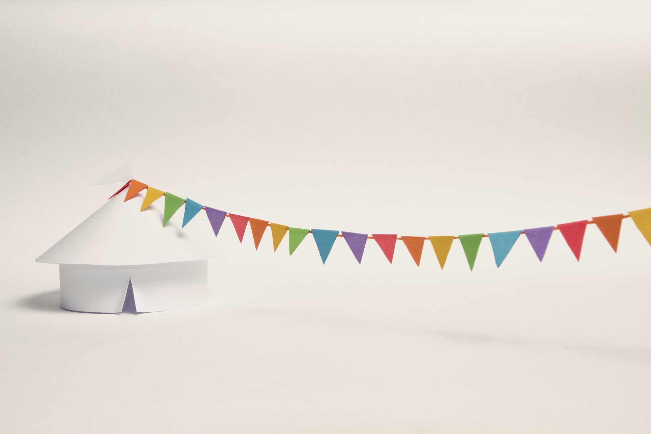 The image of a hand-made white paper circus tent with a string of rainbow coloured buntings attached to it's top. (Getty Images)