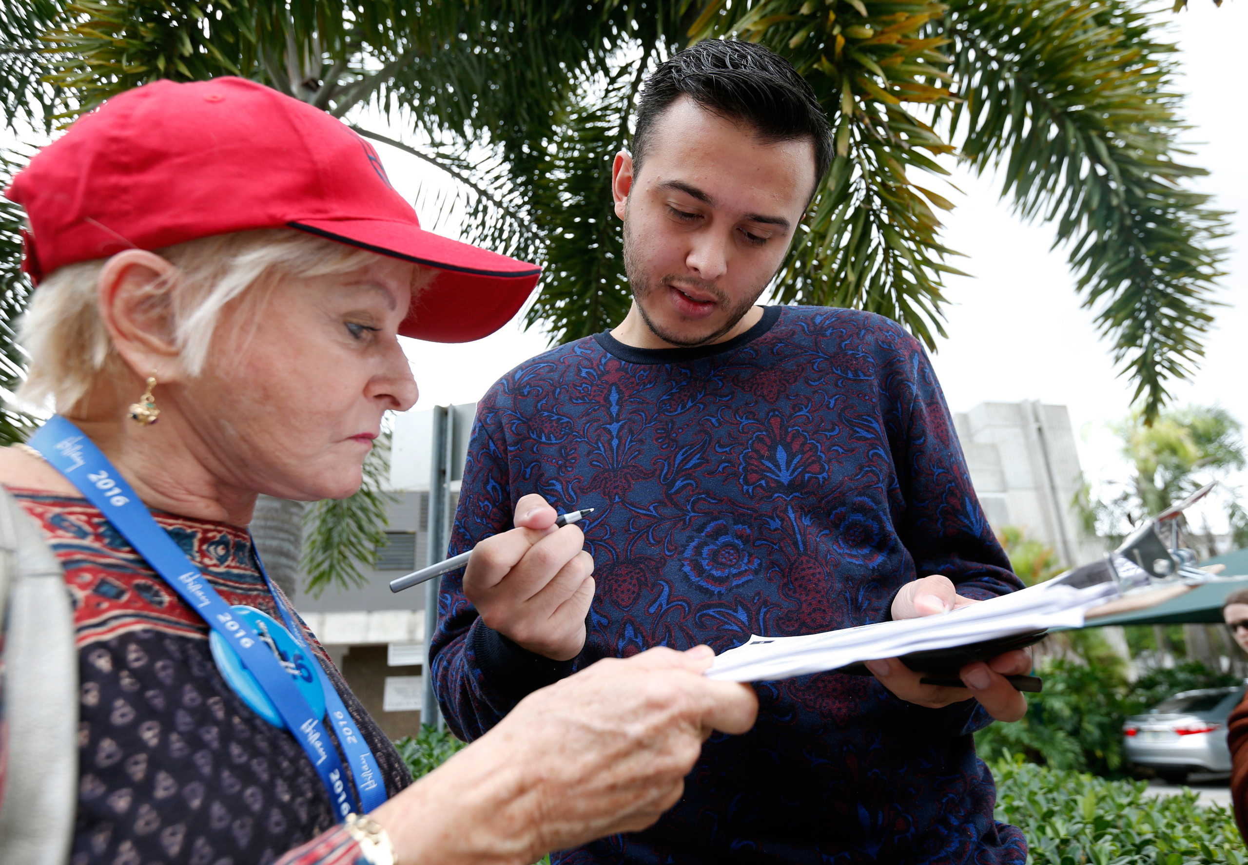 Volunteer Sandi Strickland, left, helps Roman Rodriguez, right, fill out a new voter registration form because of a change of address, as he waits in line to attend a rally for Democratic presidential candidate Hillary Clinton and former vice president Al Gore, Tuesday, Oct. 11, 2016, in Miami. A federal judge has given Democrats a partial victory in the presidential battleground of Florida, extending the state's voter registration deadline one day and agreeing to consider a longer extension in the wake of Hurricane Matthew. (AP Photo/Wilfredo Lee)