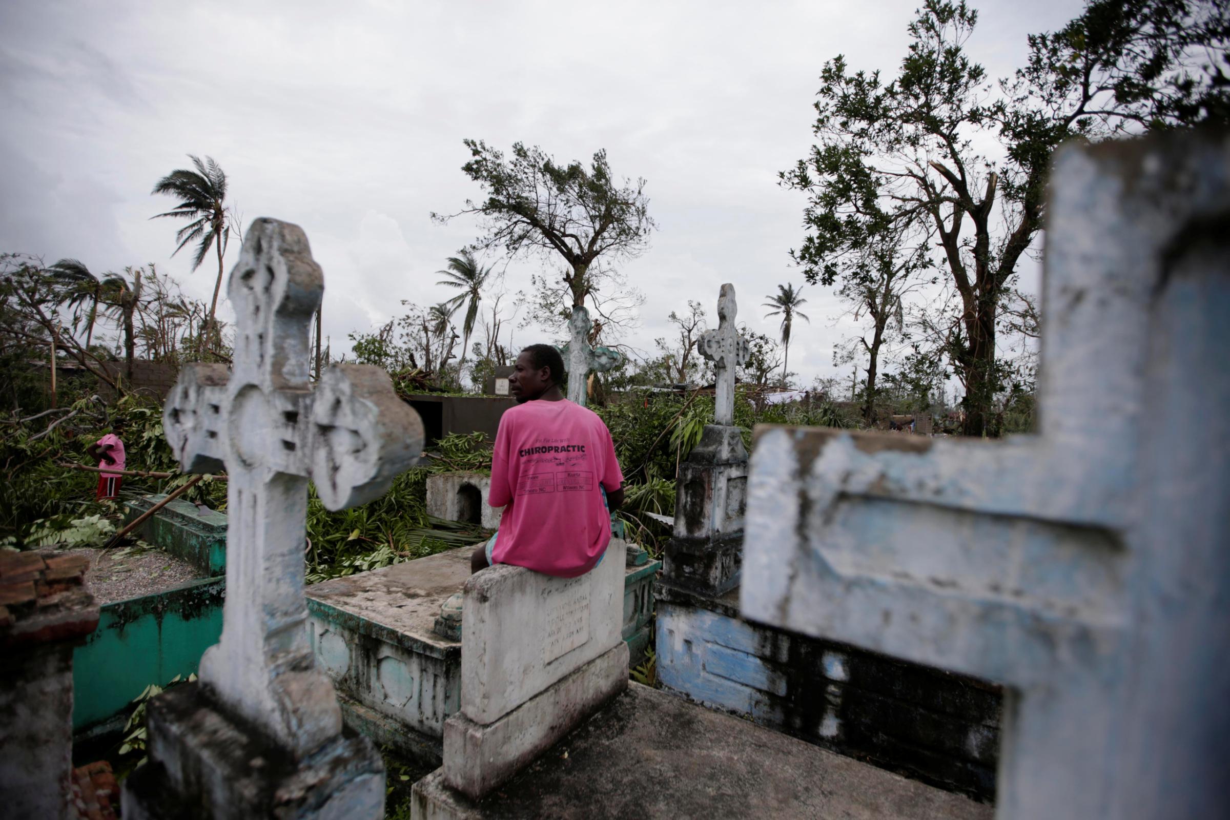 A man sits on a tombstone as he watches other clearing trees after Hurricane Matthew in Les Cayes, Haiti, October 6, 2016. REUTERS/Andres Martinez Casares - RTSR31K