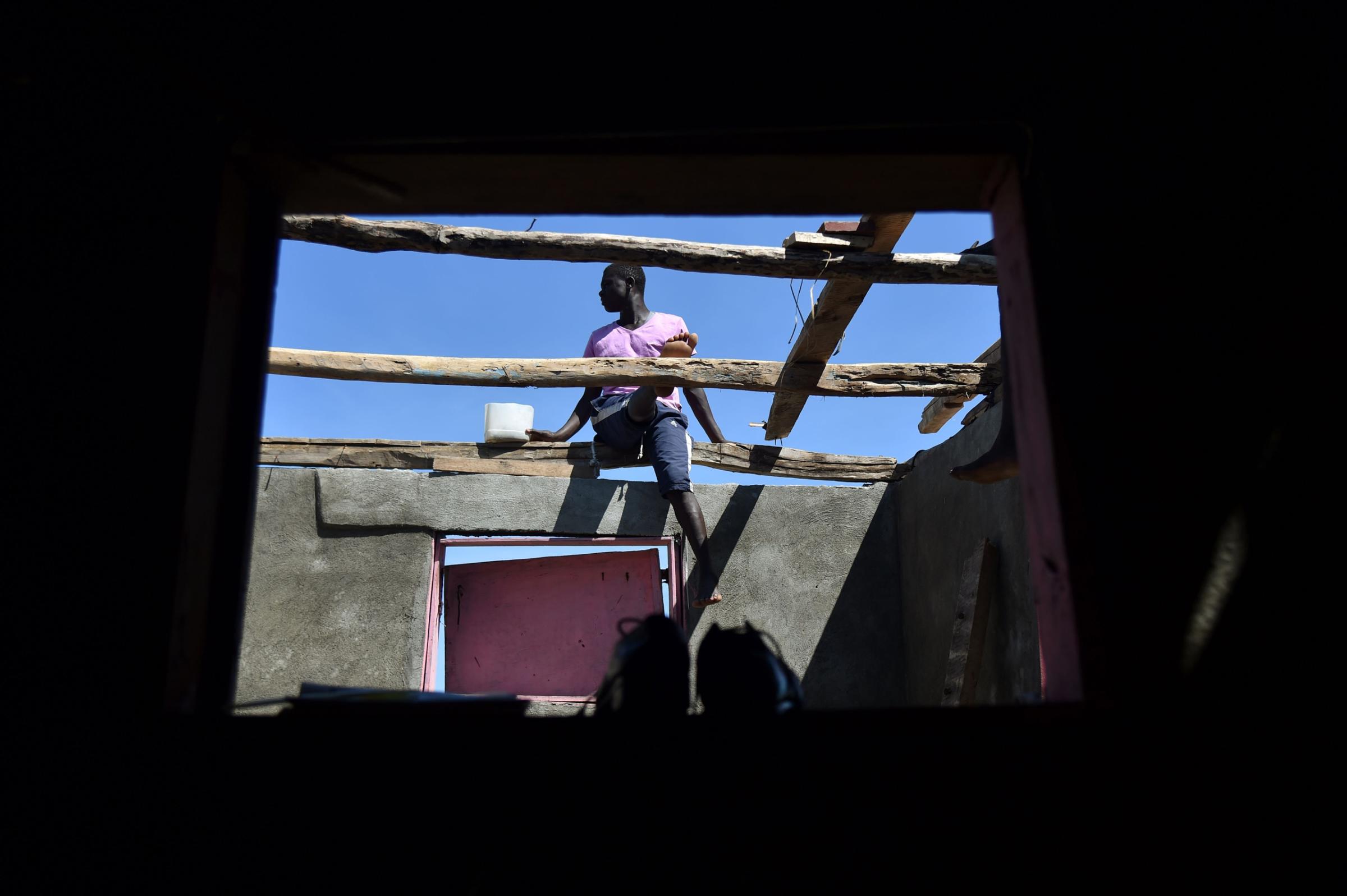 Members of a family repair their home damaged by Hurricane Matthew in Gomier, Haiti, on October 8, 2016. The full scale of the devastation in hurricane-hit rural Haiti became clear as the death toll surged over 400, three days after Hurricane Matthew leveled huge swaths of the country's south. / AFP PHOTO / HECTOR RETAMALHECTOR RETAMAL/AFP/Getty Images