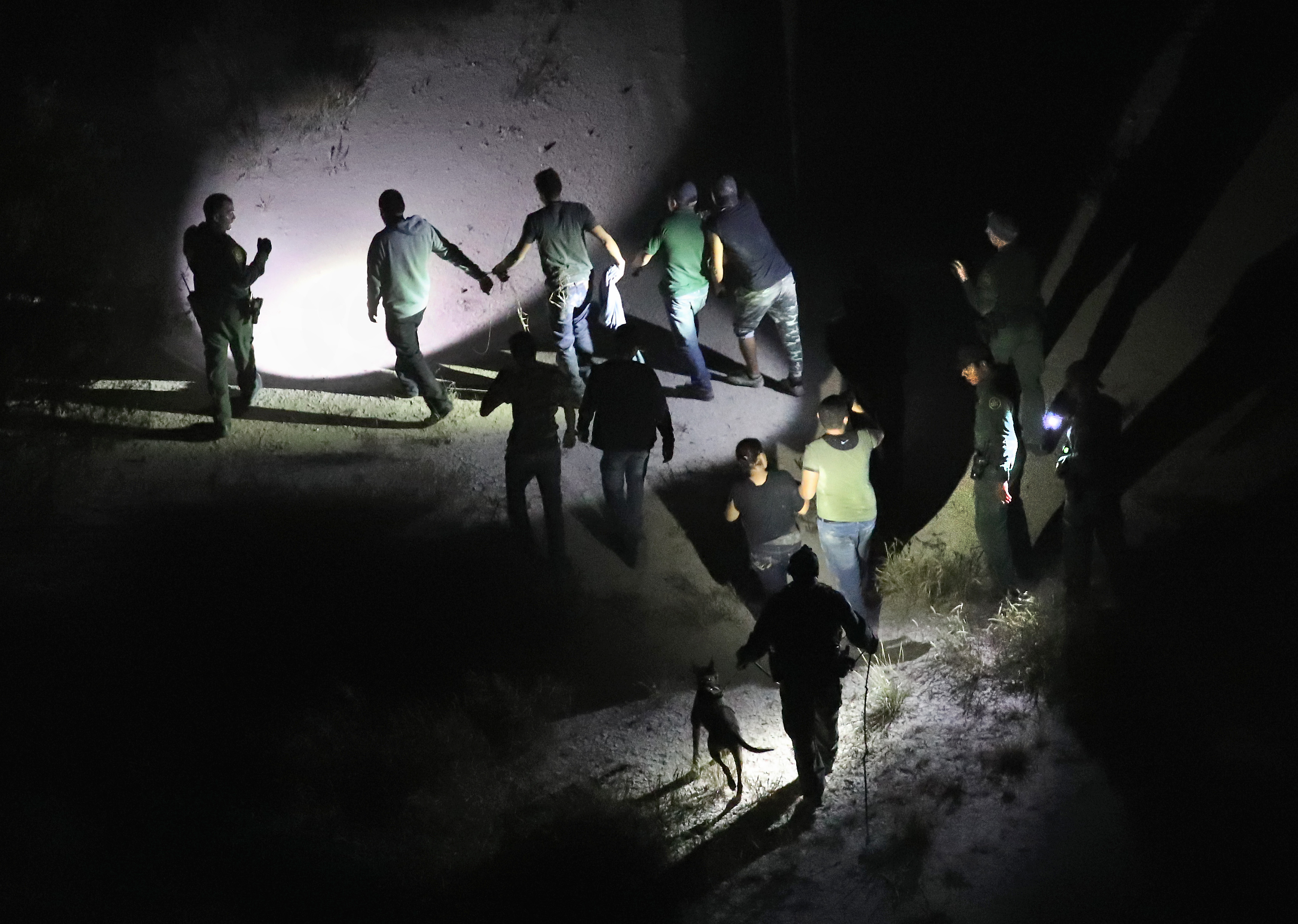 U.S. Border Patrol agents with a K-9 unit detain undocumented immigrants after they illegally crossed the U.S.-Mexico border on Oct. 18, 2016, in McAllen, Texas.