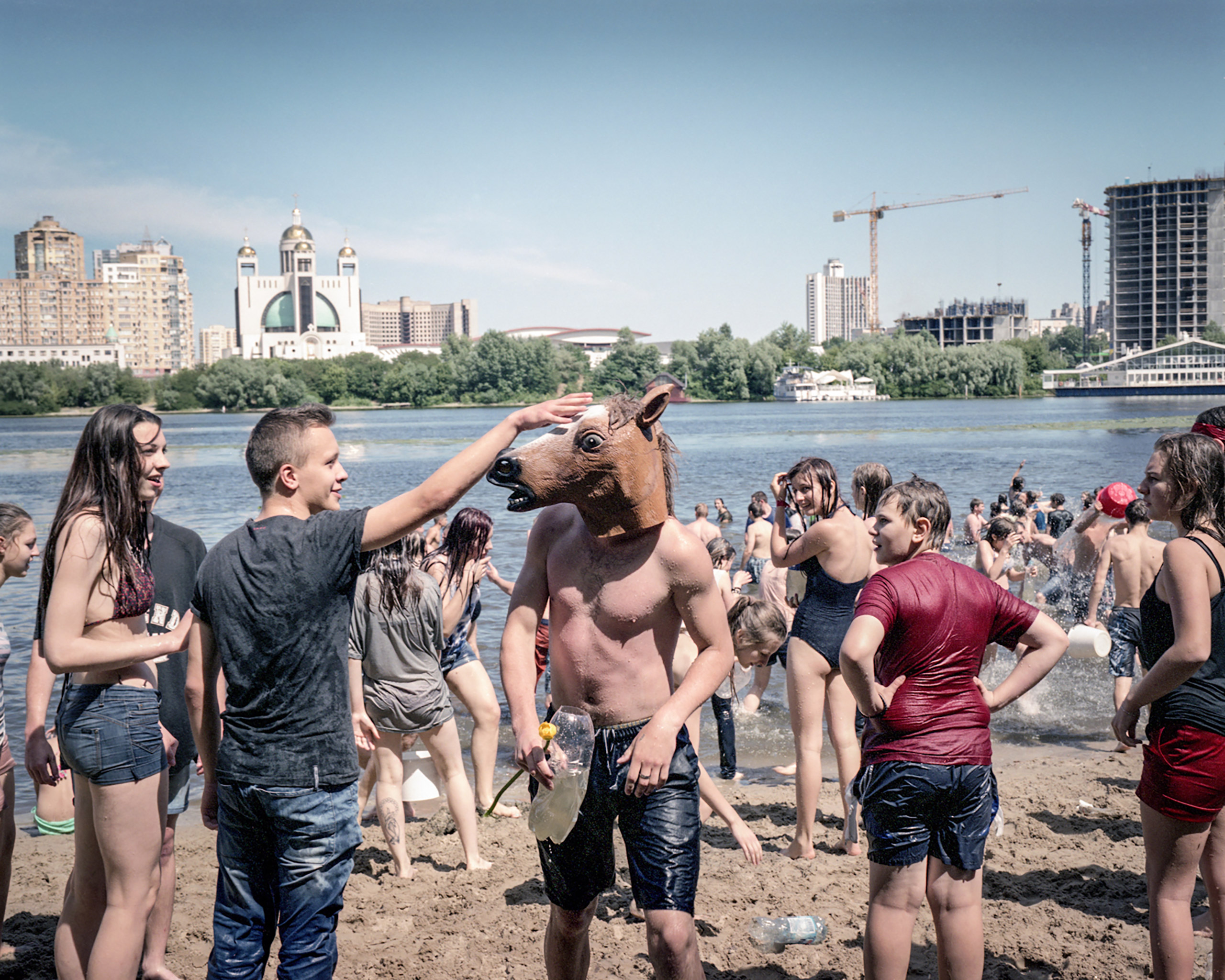 Youths play at the city beach on Dnieper River pouring water on each other. Hydropark is a landscape-recreational park on the Dnieper River. The Kiev metro station with the same name opened in 1965 and connected Hydropark Island  to the city and transformed the island to a summer resort for Kievans  Kiev, July 2015