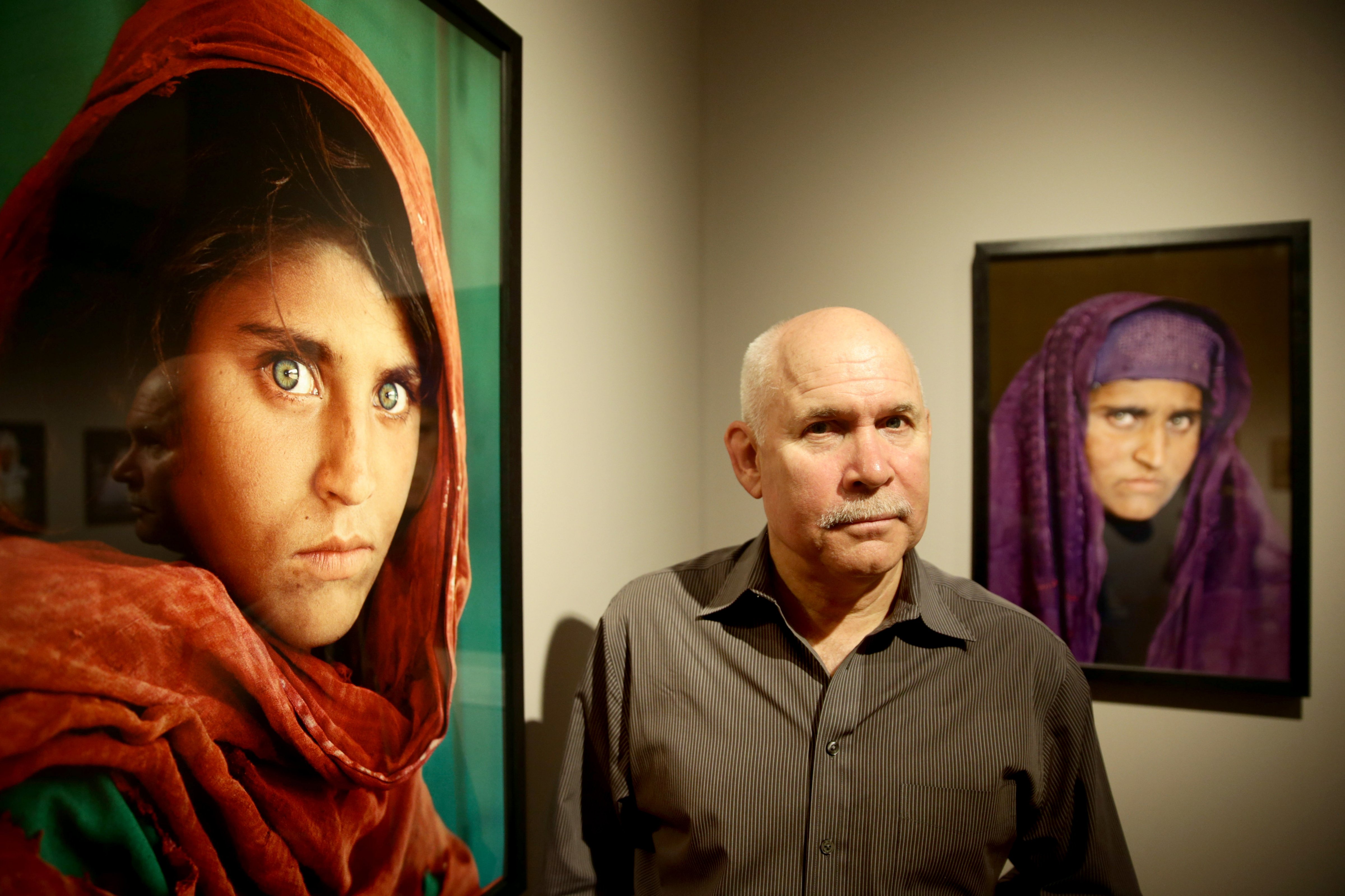 Steve McCurry poses next to his photos of the "Afghan Girl" named Sharbat Gula in Hamburg, Germany, on June 27, 2013. (Ulrich Perrey—AFP/Getty Images)