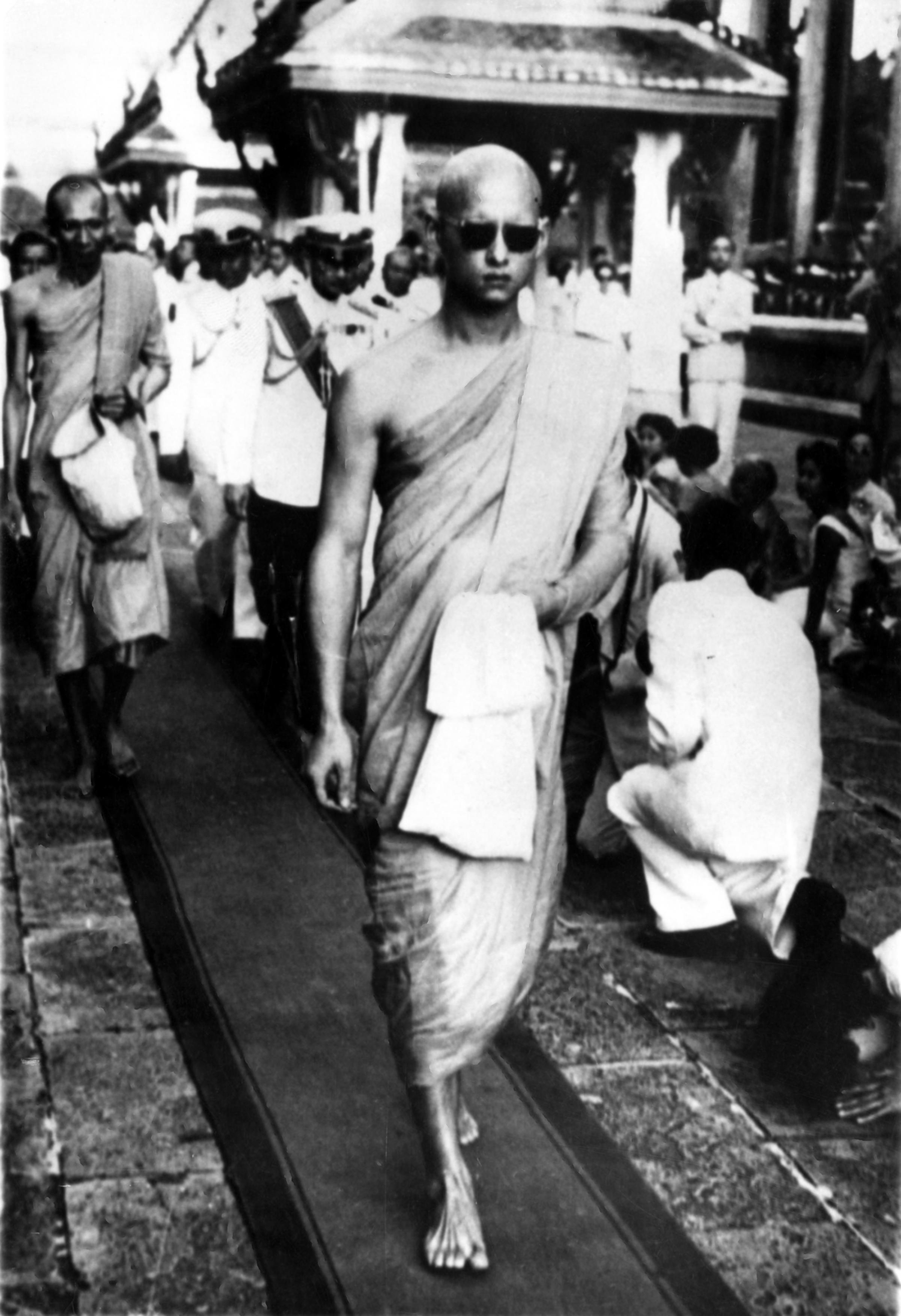 King Bhumibol Adulyadej, with head shaven and wearing the yellow robes of a monk, leaves a buddhist temple in Bangkok after being ordained a monk for two weeks in 1956.