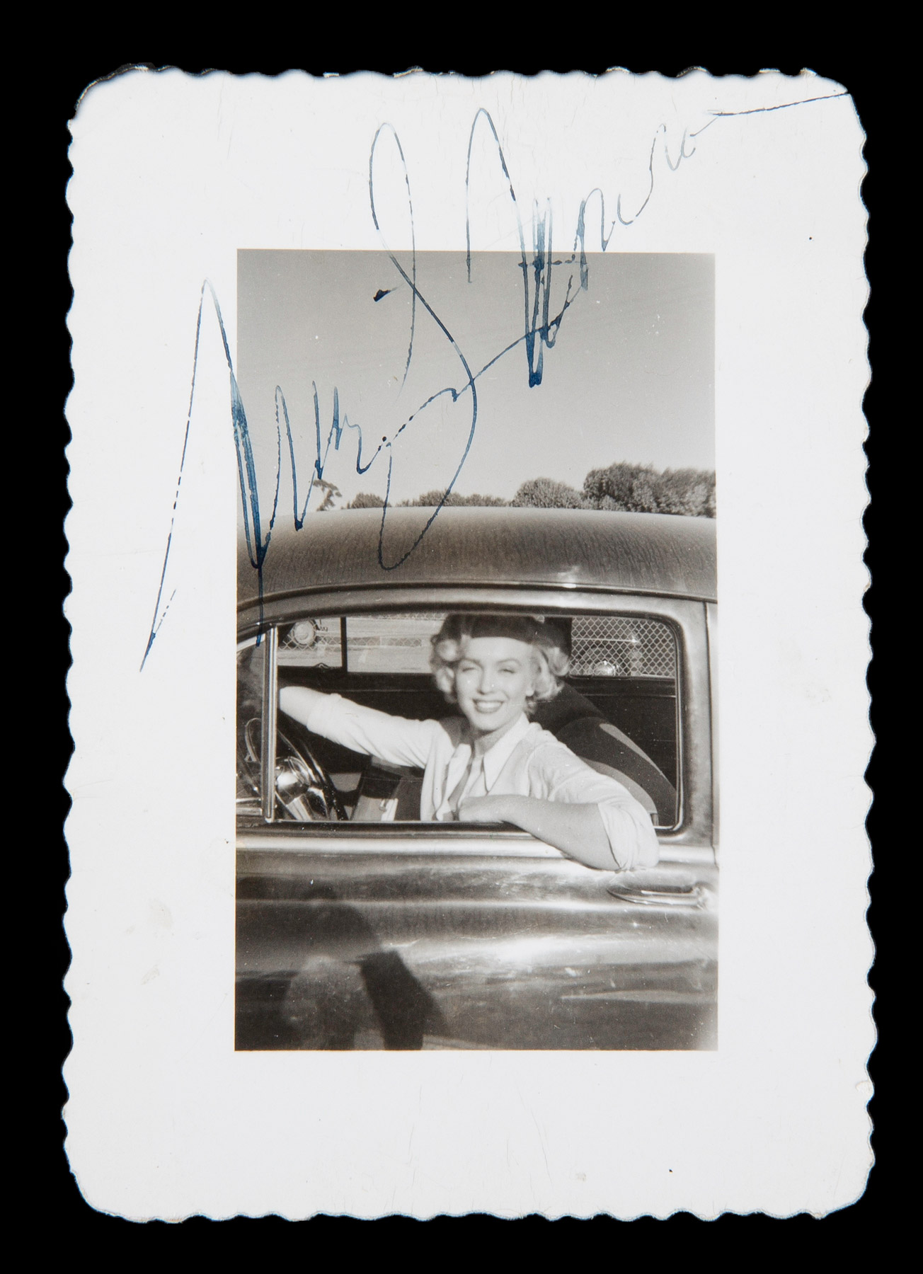 Marilyn Monroe driving a car and posing through the driver's side window taken in the mid-1950s.