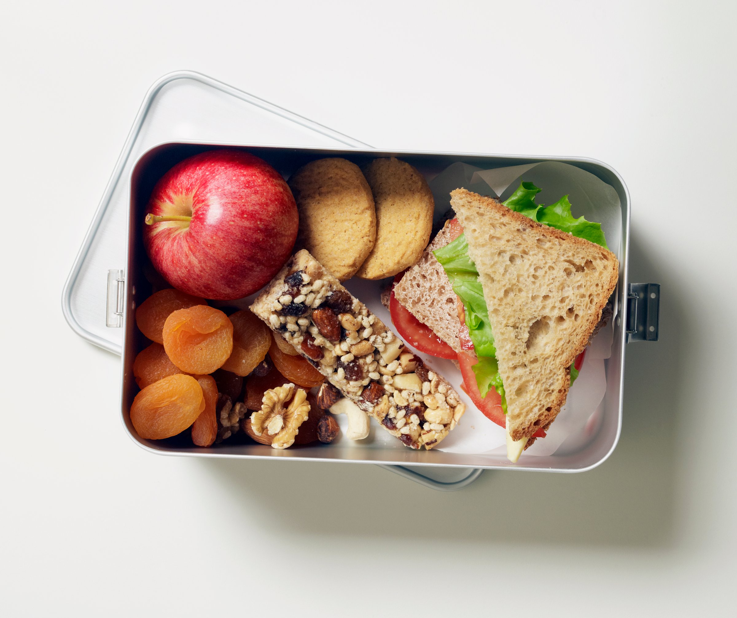 Gluten-free lunch box containing fruit, seed bar, biscuits and sandwiches