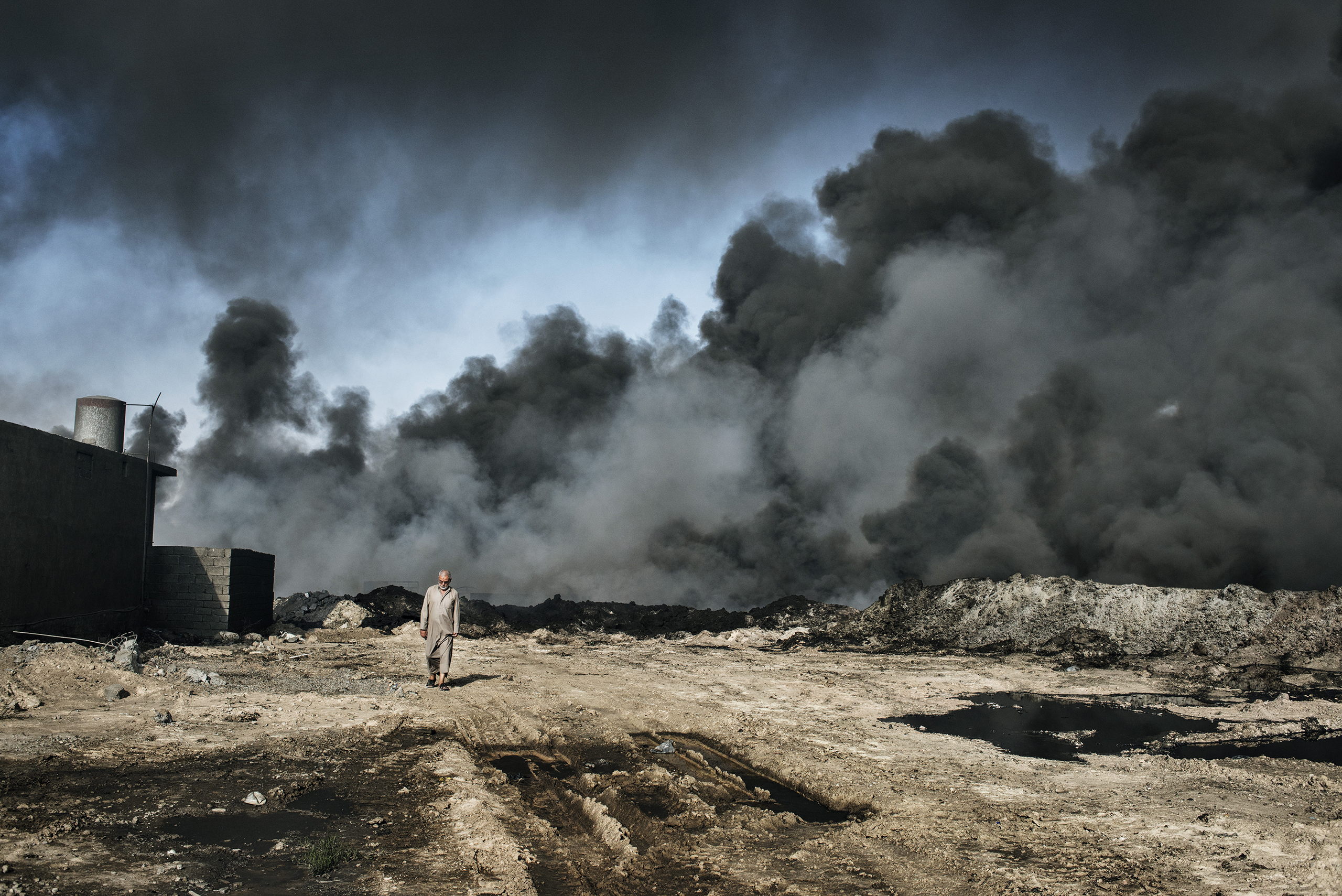 A man walks in Qayyarah, in northern Iraq, as smoke rises from a burning oil well.