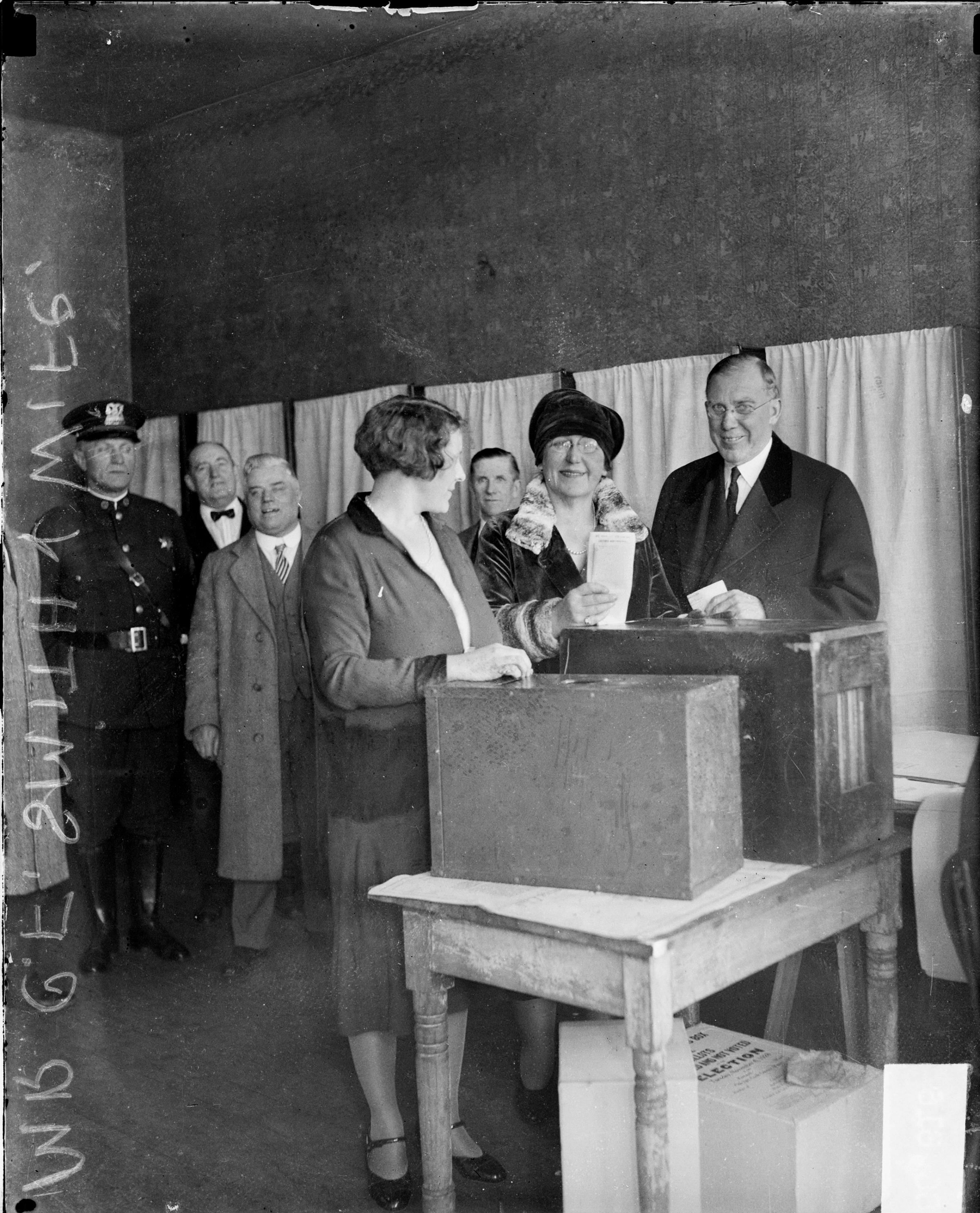 Clayton F. Smith, Deputy Commissioner of City Works, and his wife, Mayme Paschen, looking toward the camera, standing next to a ballot box at a voting poll center in Chicago, in 1928.
