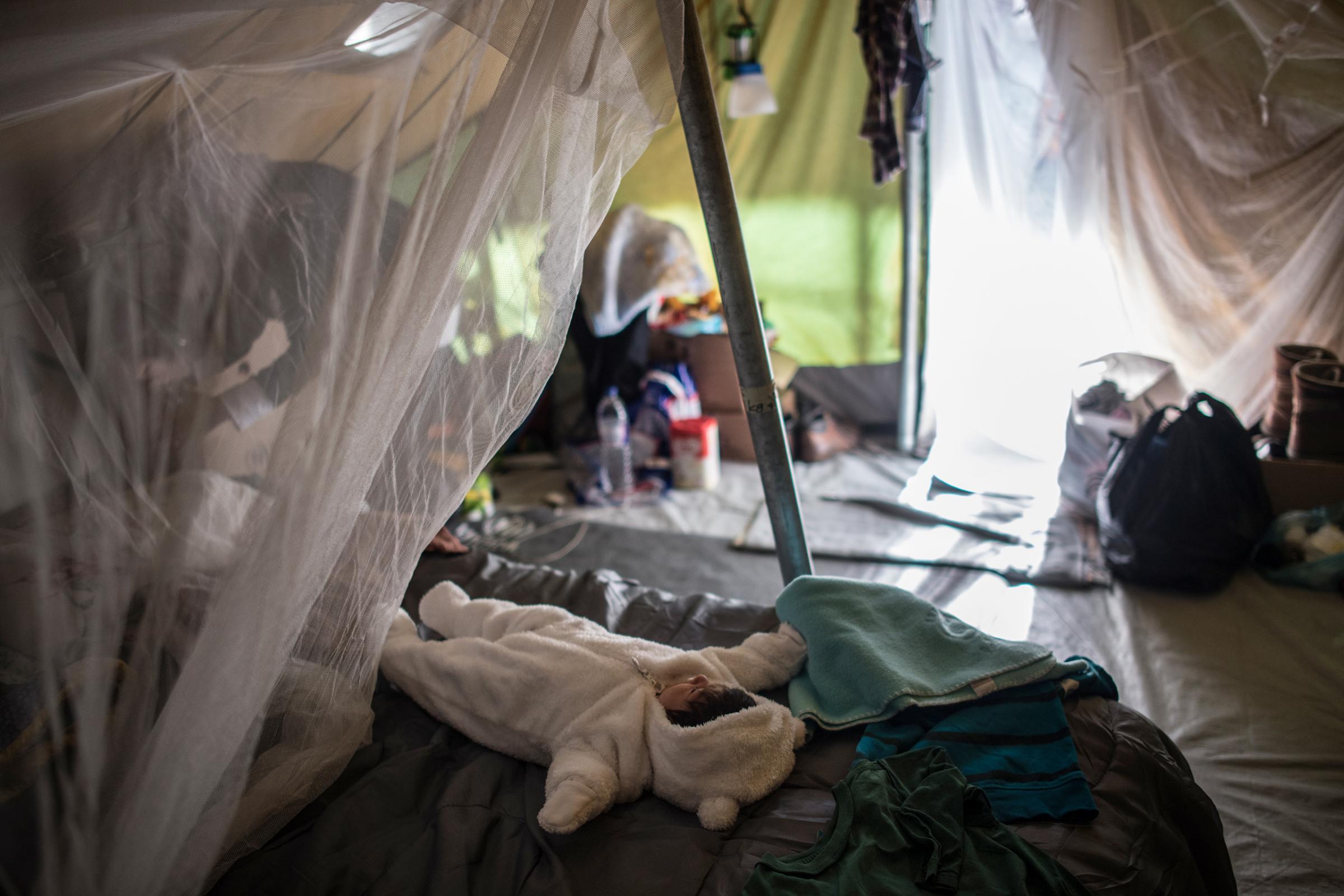 Syrian refugee Tayma Abzali, 24, straightens up her tent as her baby, Helen, born on Sept. 13, sleeps in a warm onesie at the Karamalis camp in Thessaloniki, Greece, on Nov. 10, 2016. Tayma, like other refugee mothers living in tents, is concerned about the onset of winter and cold temperatures in the tents—particularly those with new babies.