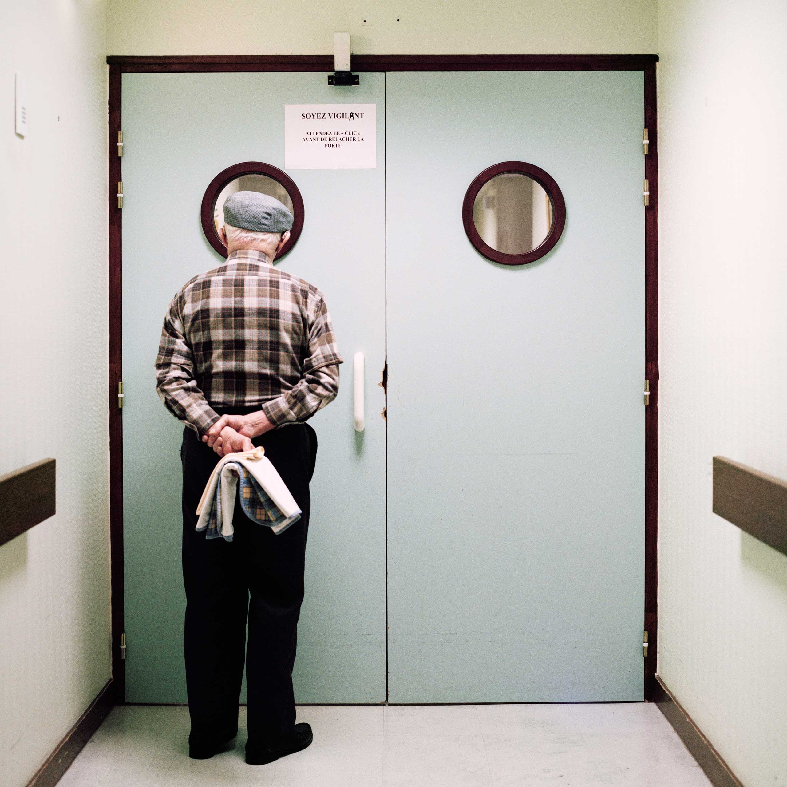 A resident stands in front of the ward’s locked exit door. Passages are blocked and doors are locked to prevent residents from wandering off.