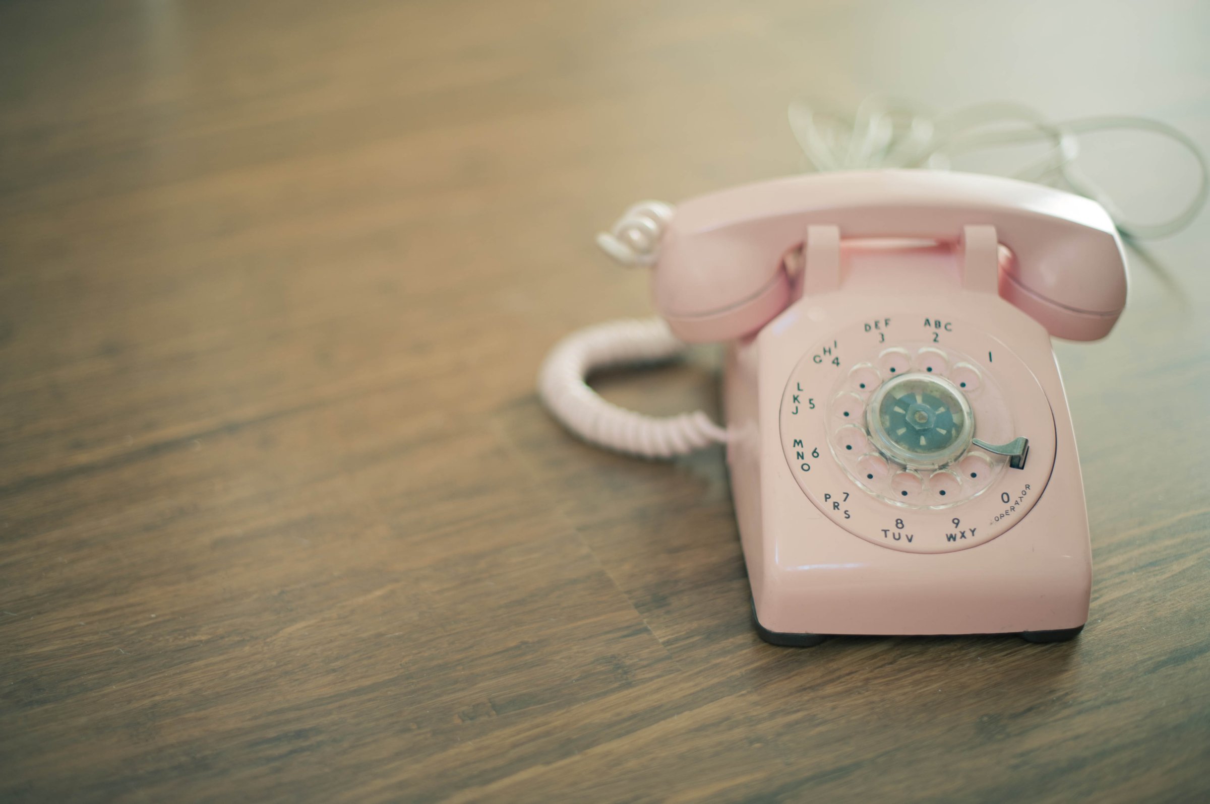 Pink rotary telephone on wood surface.