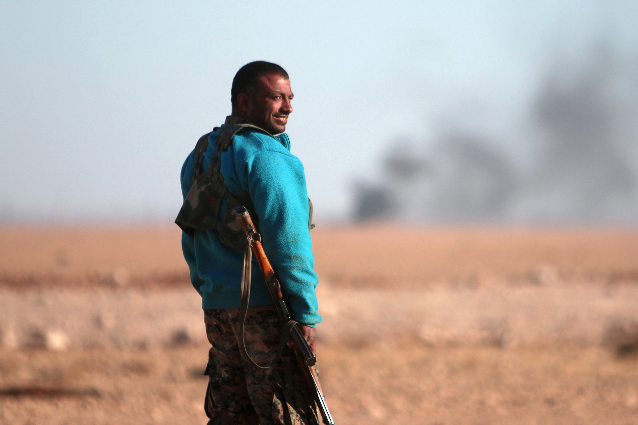 A Syrian Democratic Forces (SDF) fighter stands near rising smoke, north of Raqqa city