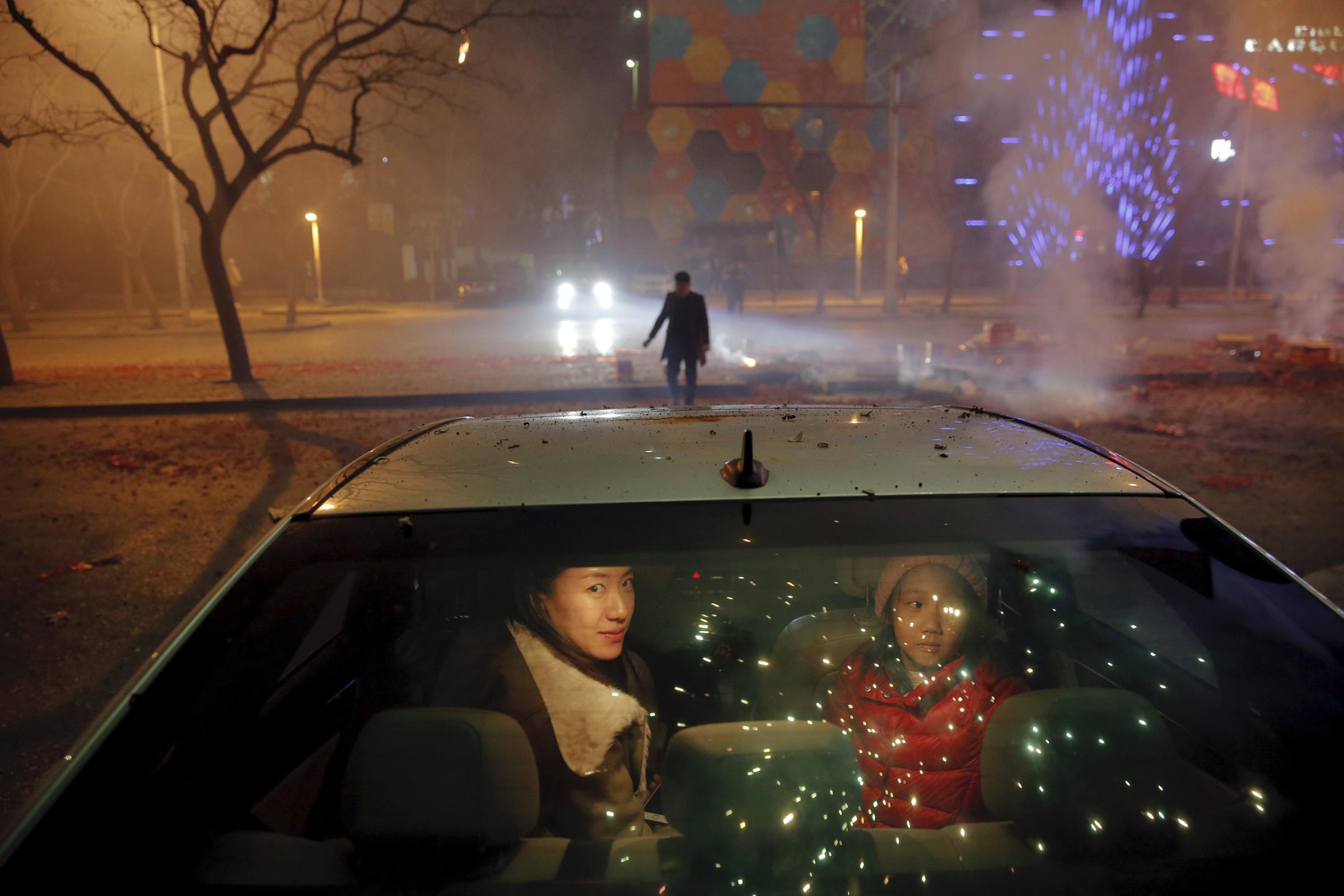 A girl and a woman sit inside the car as firecrackers and fireworks explode celebrating the start of the Chinese Lunar New Year of Monkey in Beijing