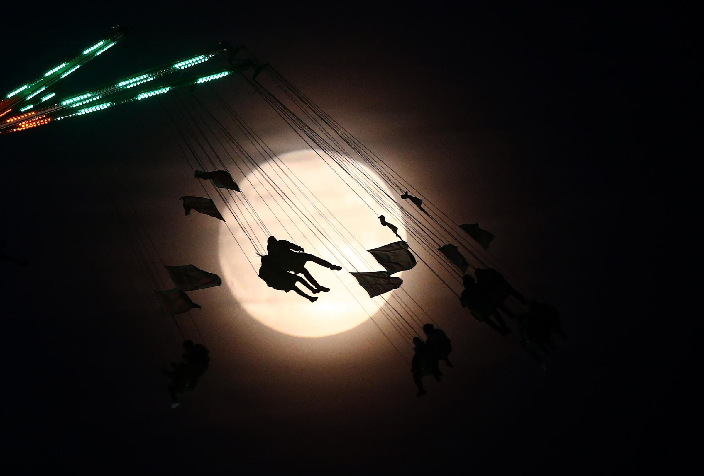 People on a funfair ride are silhouetted against the moon a day before the "supermoon" spectacle, in London