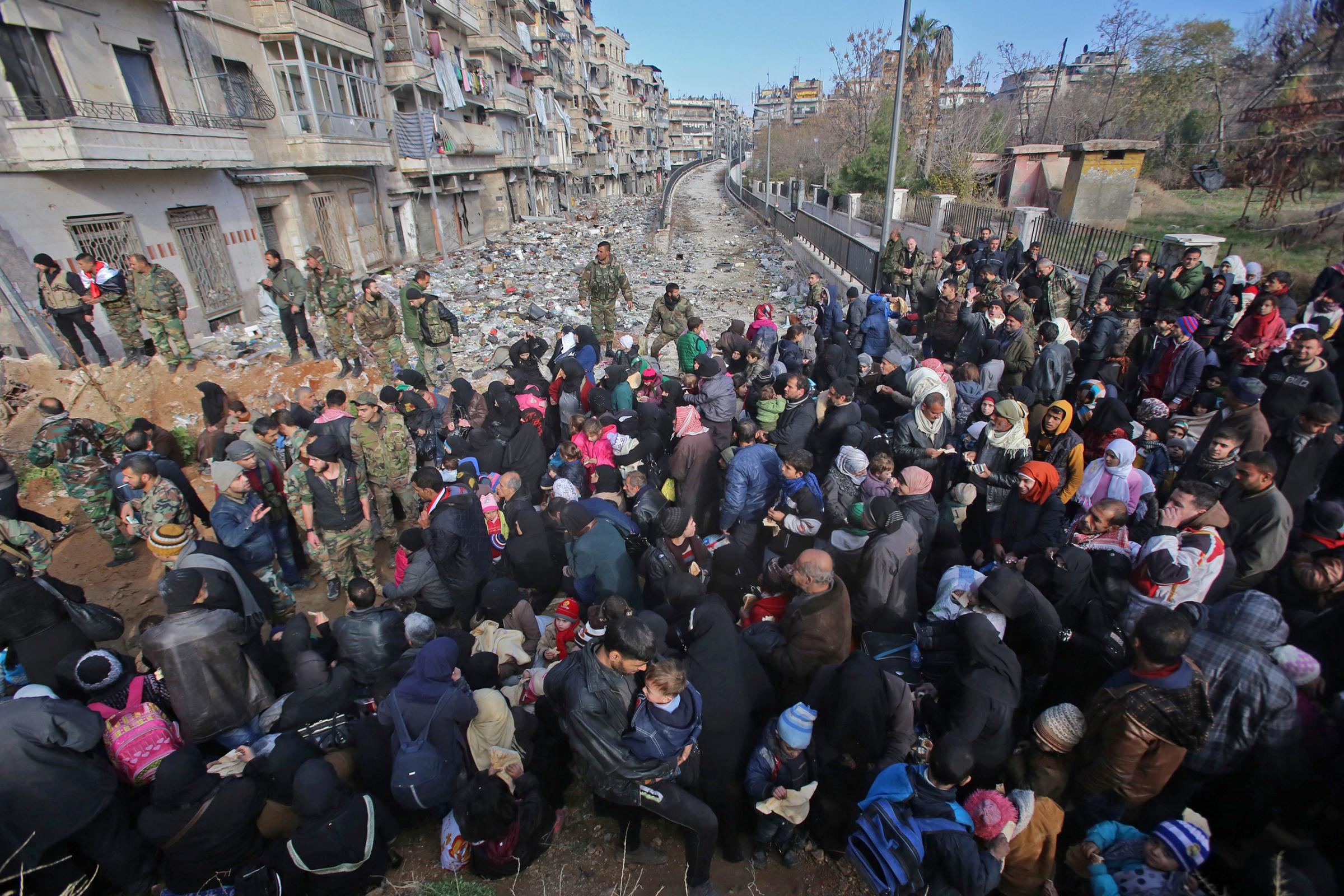 Residents fleeing the violence gather at a checkpoint, manned by pro-government forces, in the Maysaloun neighborhood of Aleppo on Dec. 8, 2016.