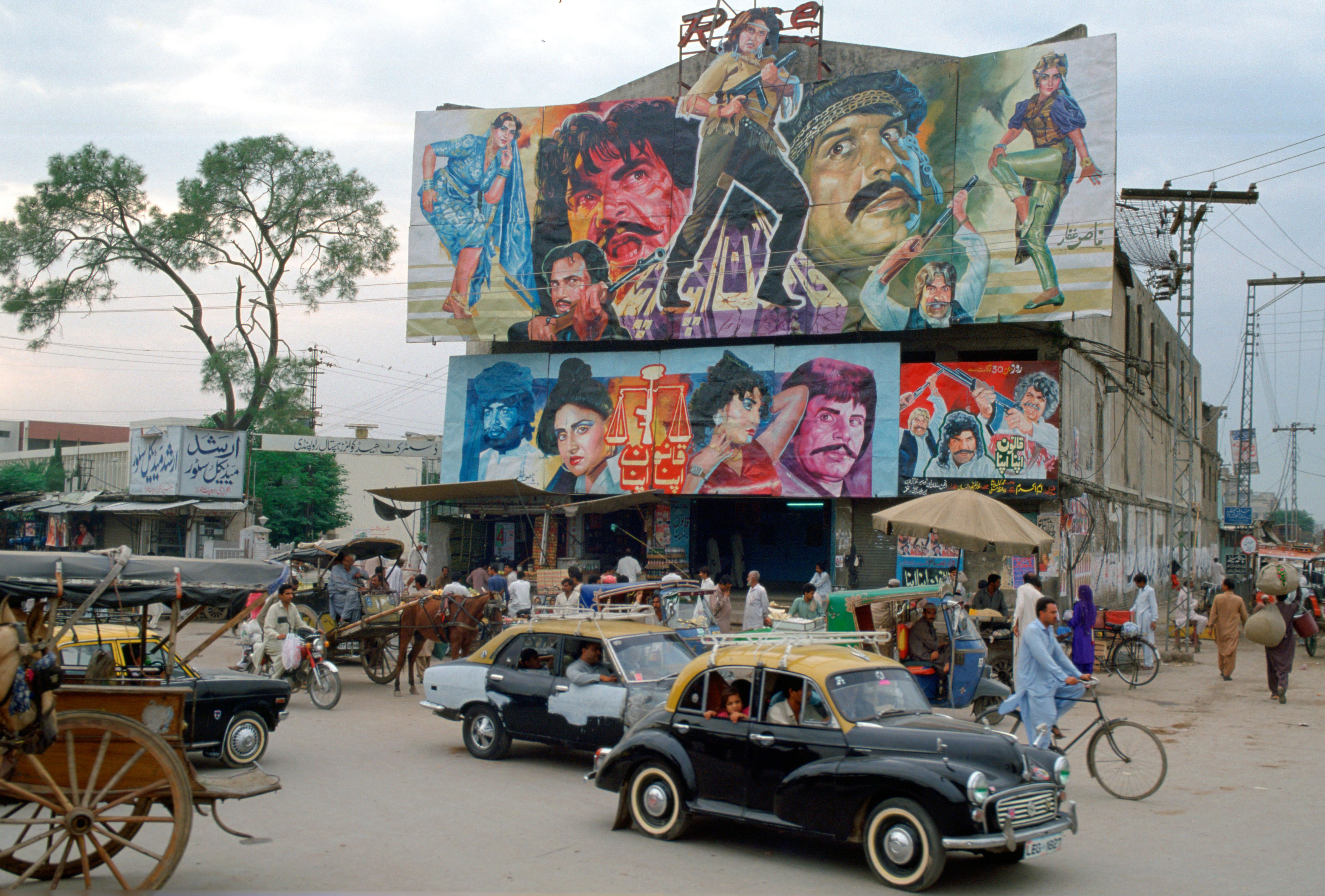 Street scene in Islamabad, Pakistan showing rickshaws, an old two-tone Morris Minor car and the local cinema advertising films often described as 
