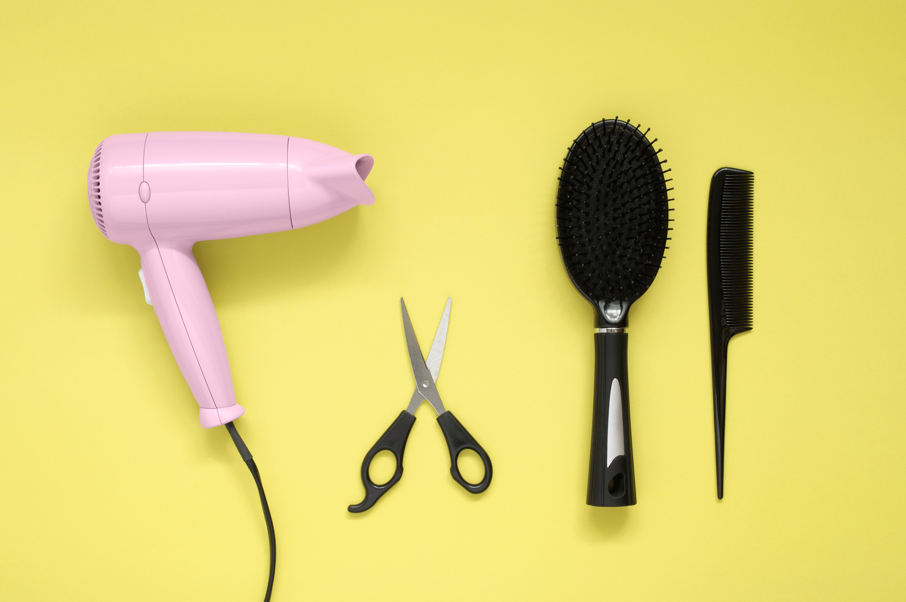 Pink hair dryer black brush, comb and scissors on yellow paper background (Vonschonertagen&mdash;Getty Images/iStockphoto)