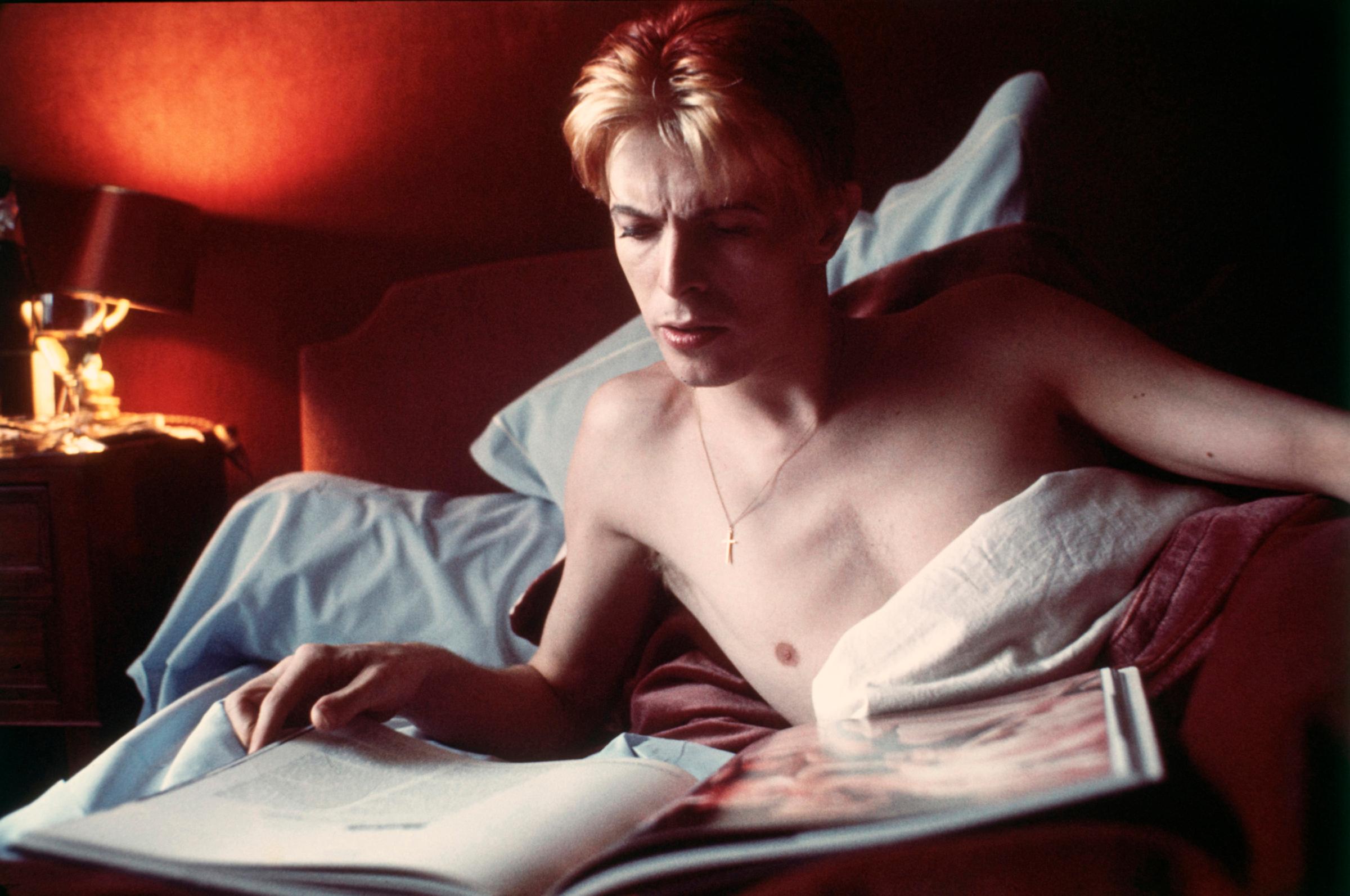 Bowie reading in bed at L'Hotel in Paris, France, 1976.
