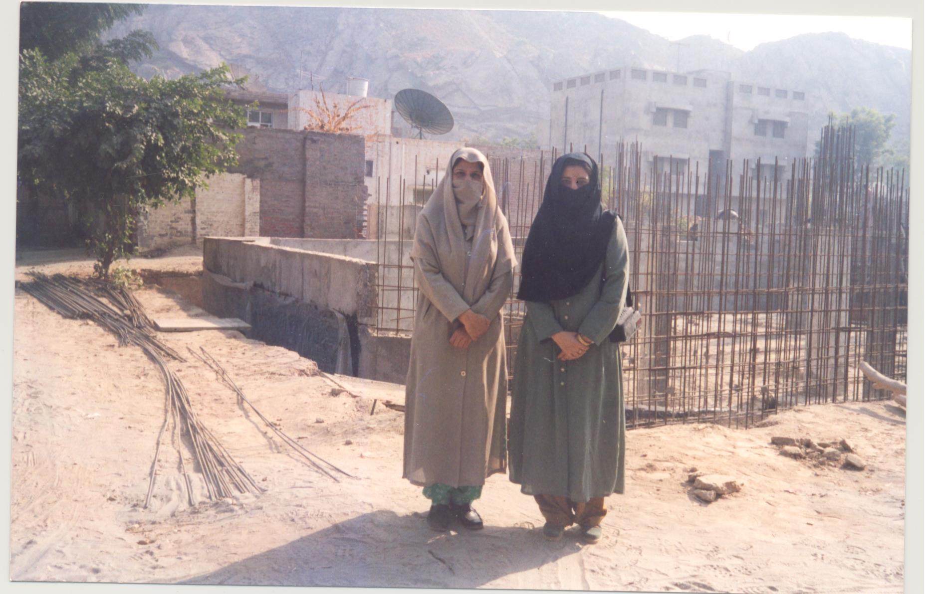 Courtesy of Dr. Nusrat Majoka, Rabwah, Pakistan. (Dr. Nusrat Jahan (left) and Dr. Amtul Haye (right) stand in front of the construction of the Begum Zubaida Bani gynecology wing of Fazl-e-Omer hospital in Rabwah, Pakistan, in 2002.)
