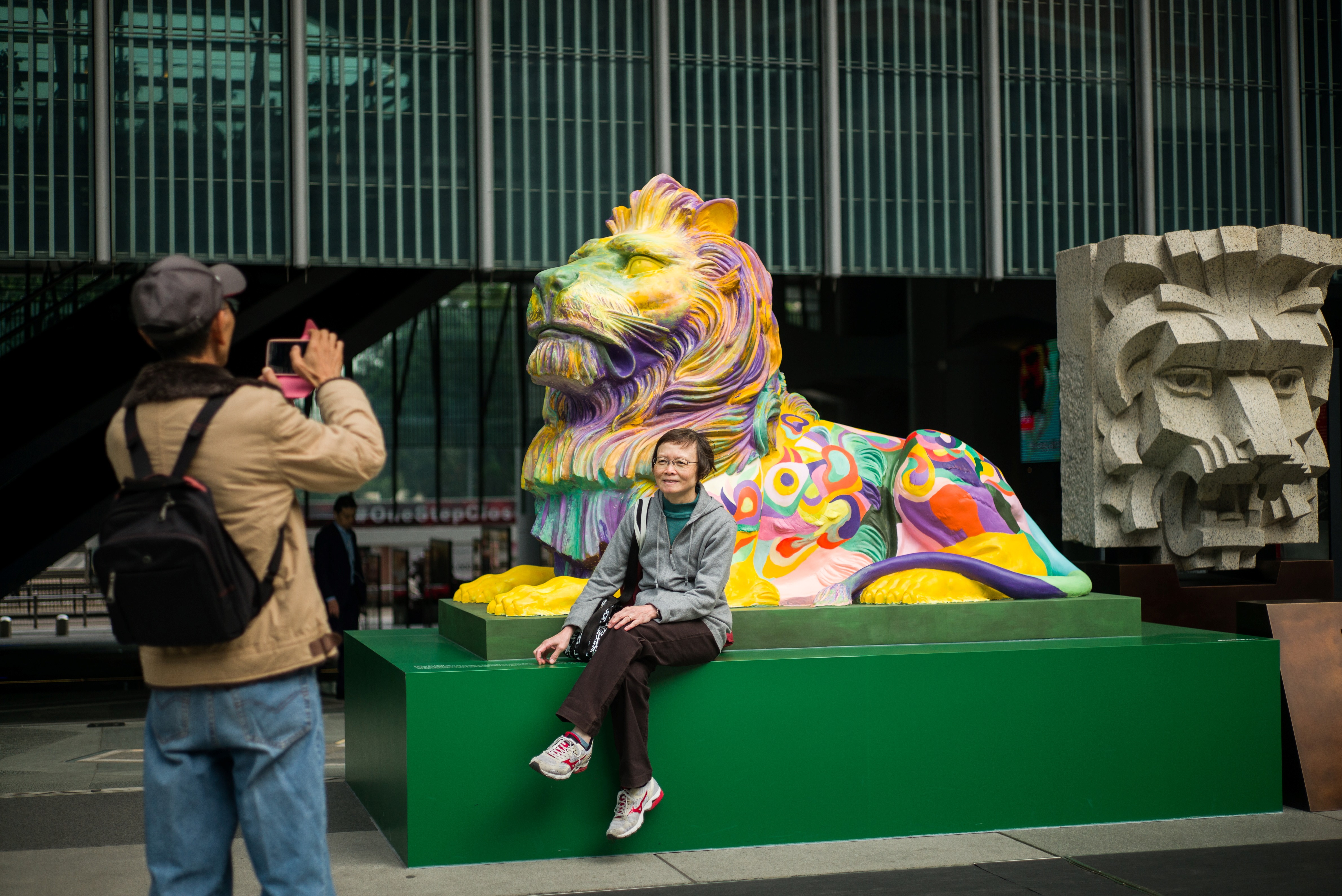 A man takes a photo of his wife as she poses in front of a lion painted in rainbow stripes outside HSBC's main office in Hong Kong on Dec. 6, 2016 (Anthony Wallace—AFP/Getty Images)
