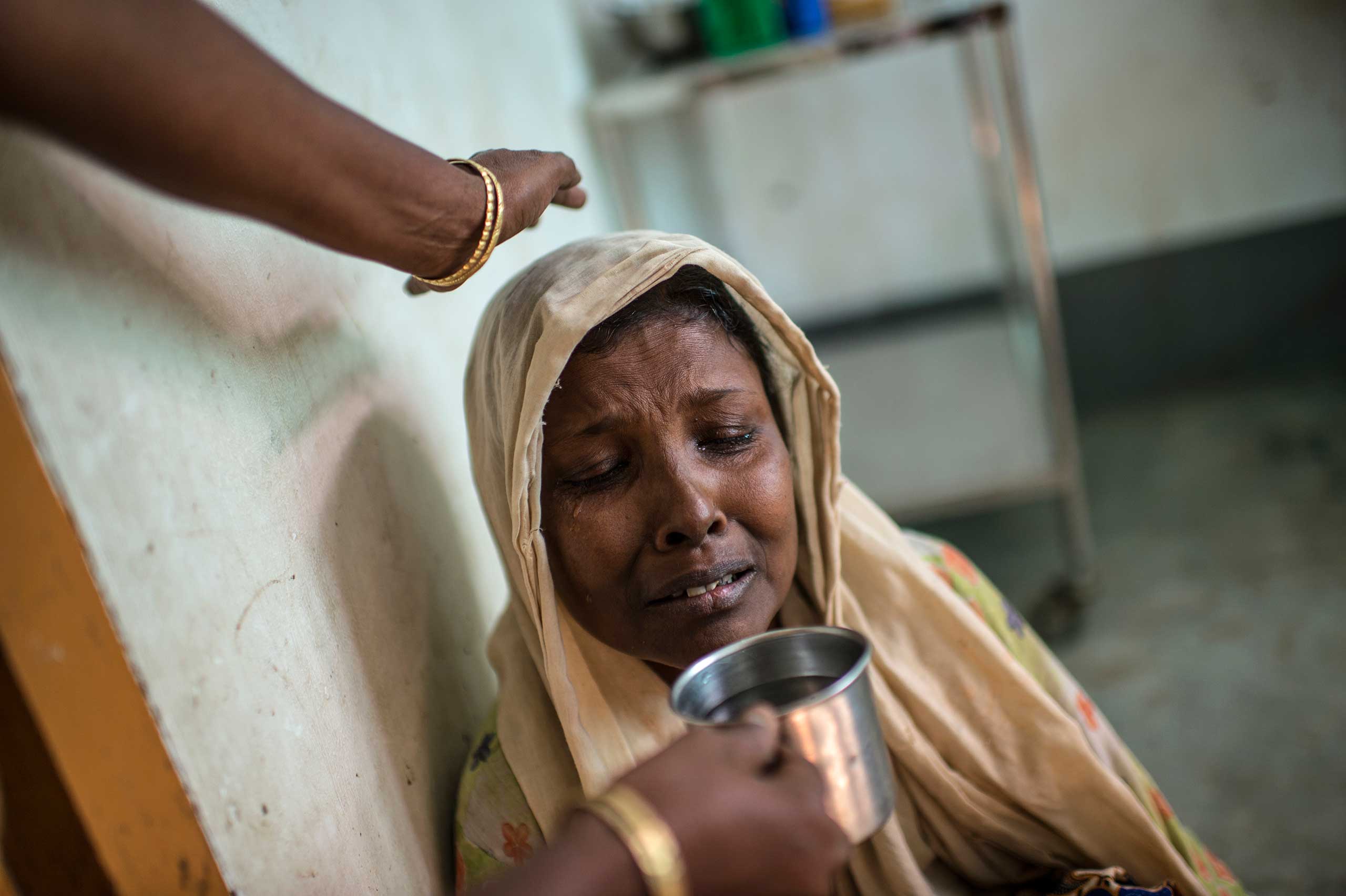 Moriam Katu, 50 years, who is gravely ill from severe asthma, is offered water as she struggles to breathe in the That Kay Pin Emergency Hospital in the camp for Internally Displaced Rohingya outside of Sittwe, in Myanmar, Nov. 25, 2015.  Moriam was so ill, she could barely breathe, and began coughing up blood. She visited the emergency hospital at the That Kay Pin within the IDP camp, and there were not sufficient resources to treat her there. The medical advisor offered to transfer her to the government hospital in Sittwe, but she declined, because her family did not have enough money to keep her there.  While her medical treatment would be free, her guardian would need to pay for food, which they estimated would be 20-30000 for food for a week. She declined and went back home. A few days later, she returned, and was transferred to Sittwe hospital, and died 10 days later.