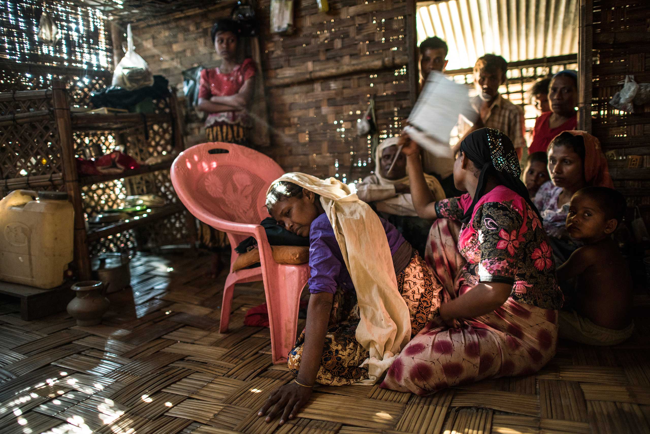 Moriam Katu, 50, who is gravely ill from severe asthma, is comforted by her daughters and other loved ones in the Ba Du Paw camp for Internally Displaced Rohingya around Sittwe, in Myanmar. Moriam was so ill, she could barely breathe, and began coughing up blood.  She visited the emergency hospital at the That Kay Pin within the IDP camp, and there were not sufficient resources to treat her there. The medical advisor offered to transfer her to the government hospital in Sittwe, but she declined, because her family did not have enough money to keep her there.  While her medical treatment would be free, her guardian would need to pay for food, which they estimated would be 20-30000 for food for a week. She declined and went back home. A few days later, she returned, and was transferred to Sittwe hospital, and died 10 days later.