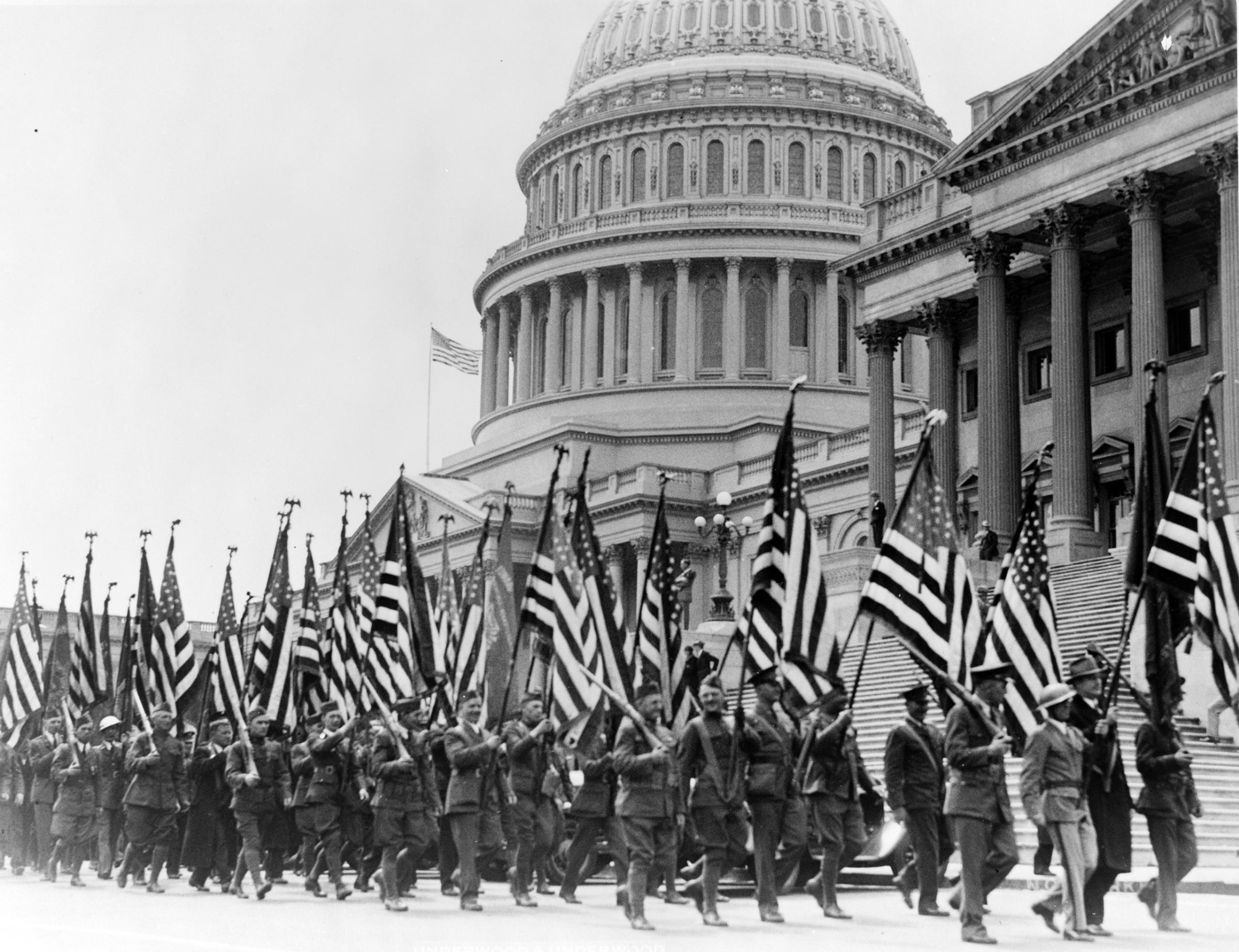 Members of the Bonus Expeditionary Forces, many carrying American flags, marching across the east plaza of the U.S. Capitol. April 8, 1932.