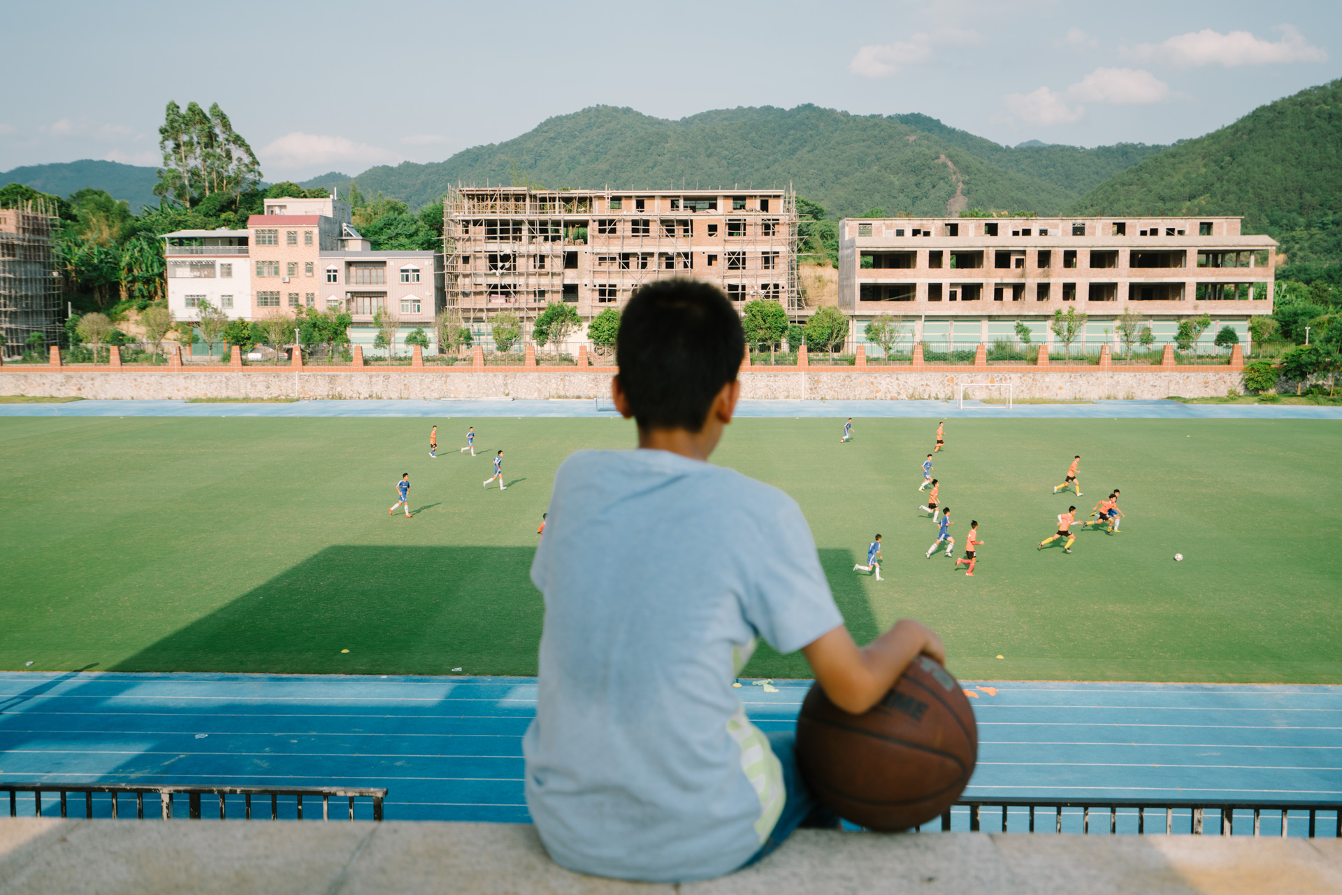 Husan, 13, watches high-school students playing football. June 3, 2016.