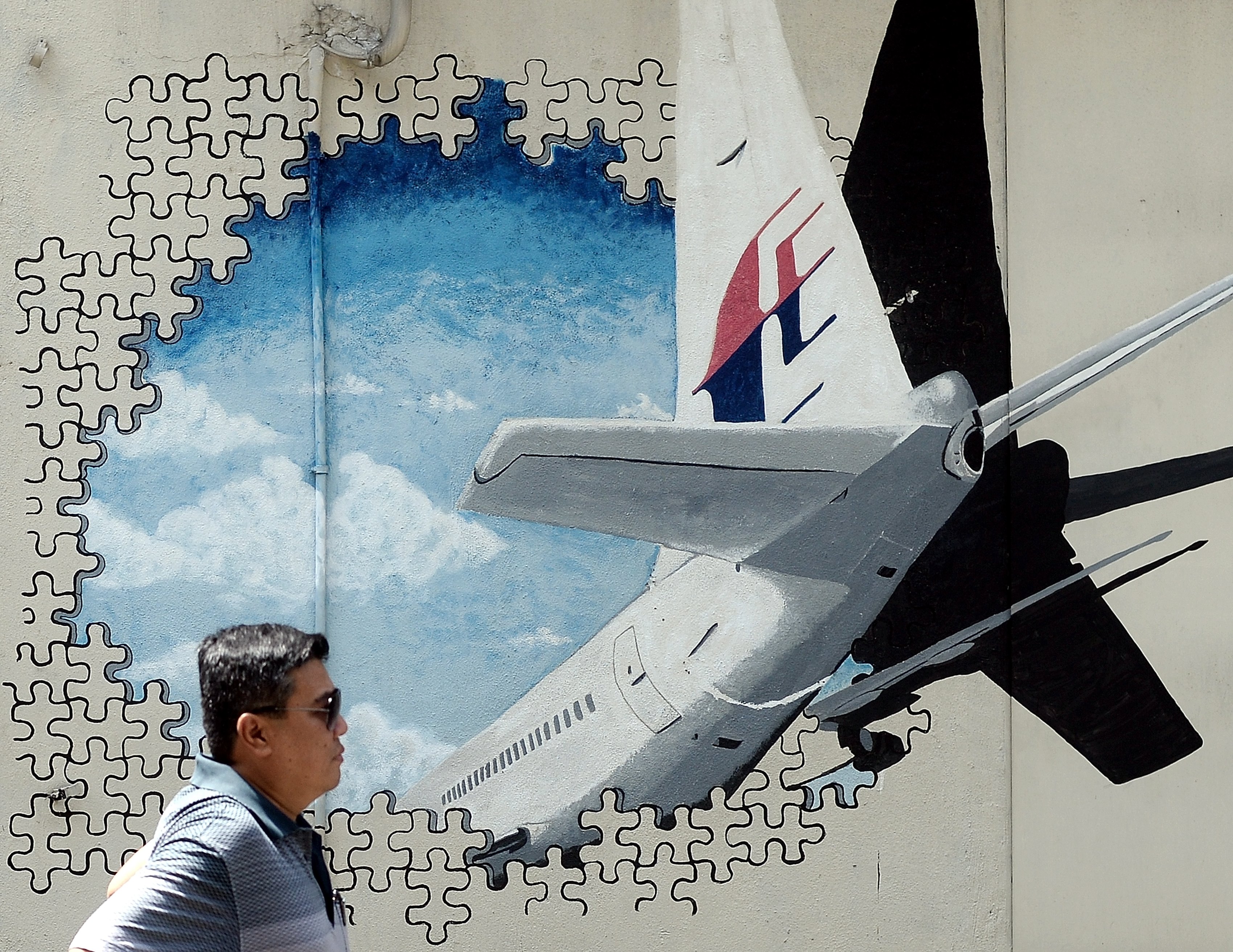 A Malaysian man walks in front of a mural of missing Malaysia Airlines MH370 plane in a back-alley in Shah Alam on March 8, 2016. (Manan Vatsyayana—AFP/Getty Images)