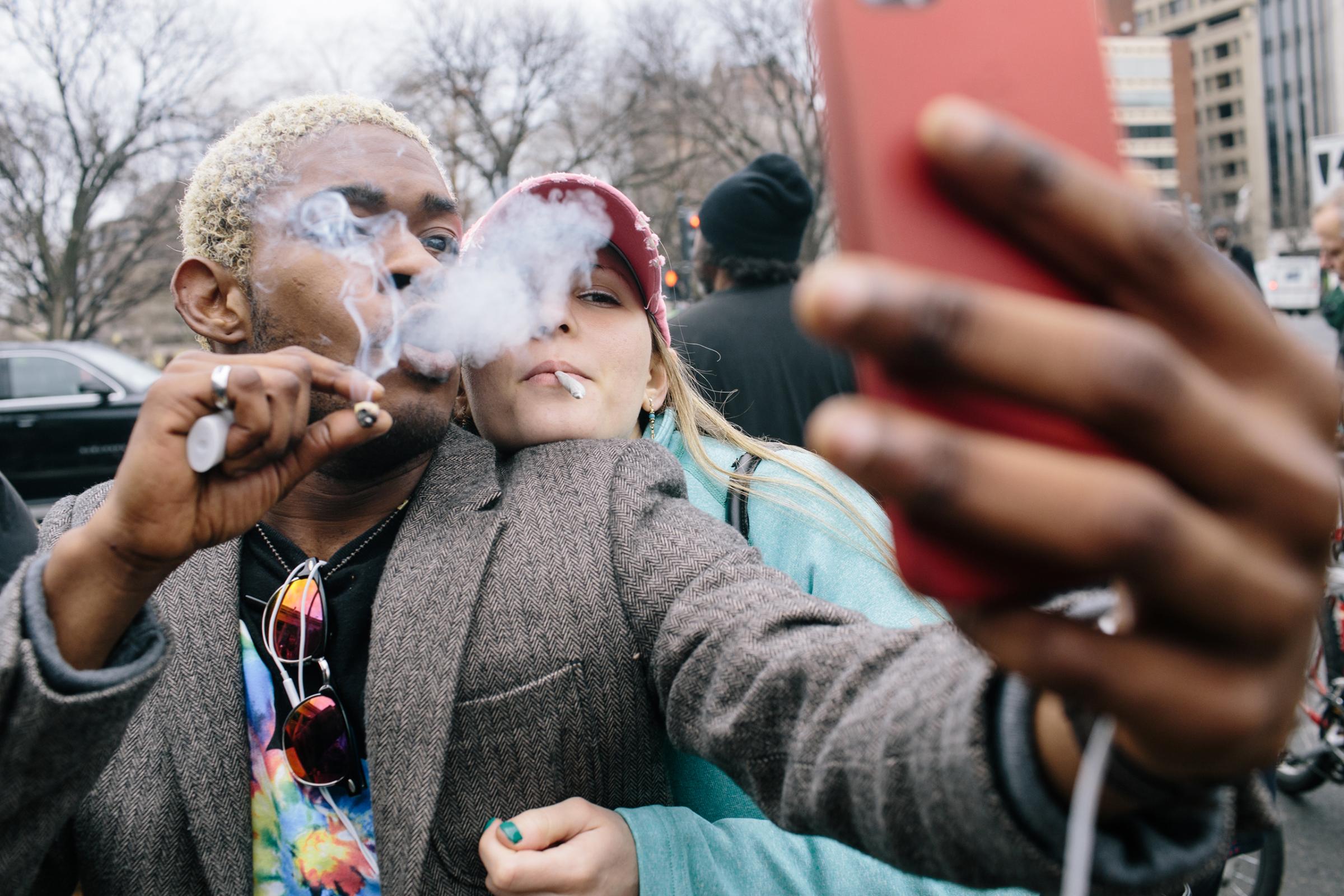 Giovanni Gopaulsingh, 25, from Maryland, and Ariel Johnson, 25, from Washington, D.C., smoke joints as they take a selfie during #Trump420 on Friday morning in Washington, D.C. An estimated 10,000 people showed up to receive a free joint given away by DCMJ near Dupont Circle on Inauguration Day, January 20, 2017 in Washington, D.C. The event was put on to bring awareness to marijuana reform.