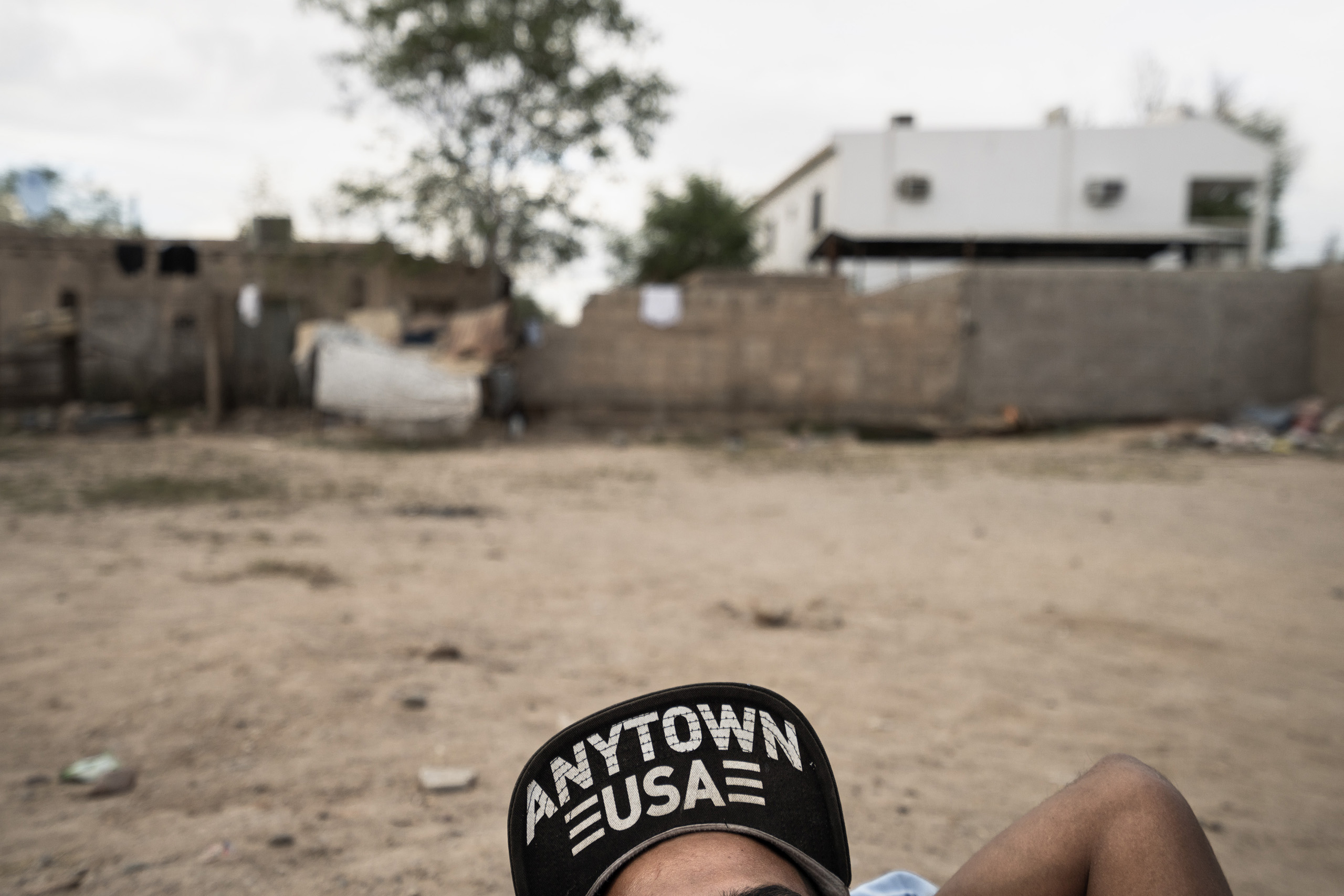 An illegal Central American migrant rests on the ground at an immigrant shelter in Caborca, a town in the state of Sonora, Mexico. His hat reads:  Anytown US.  Caborca, Sonora, Mexico. Oct. 7, 2016.