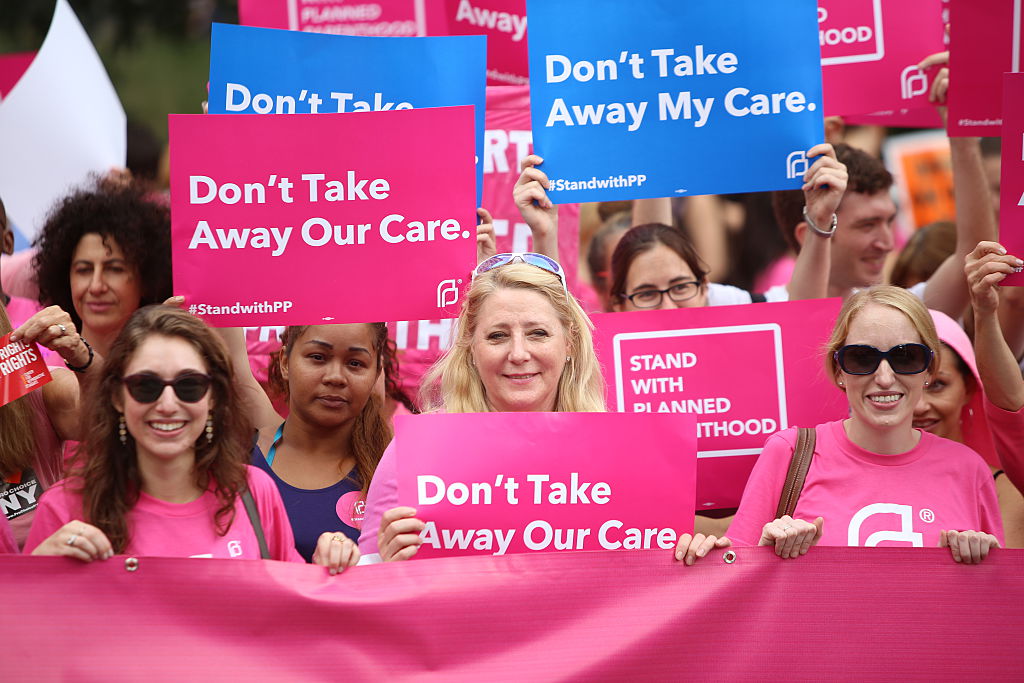 Planned Parenthood supporters hold pink banner and signs.
