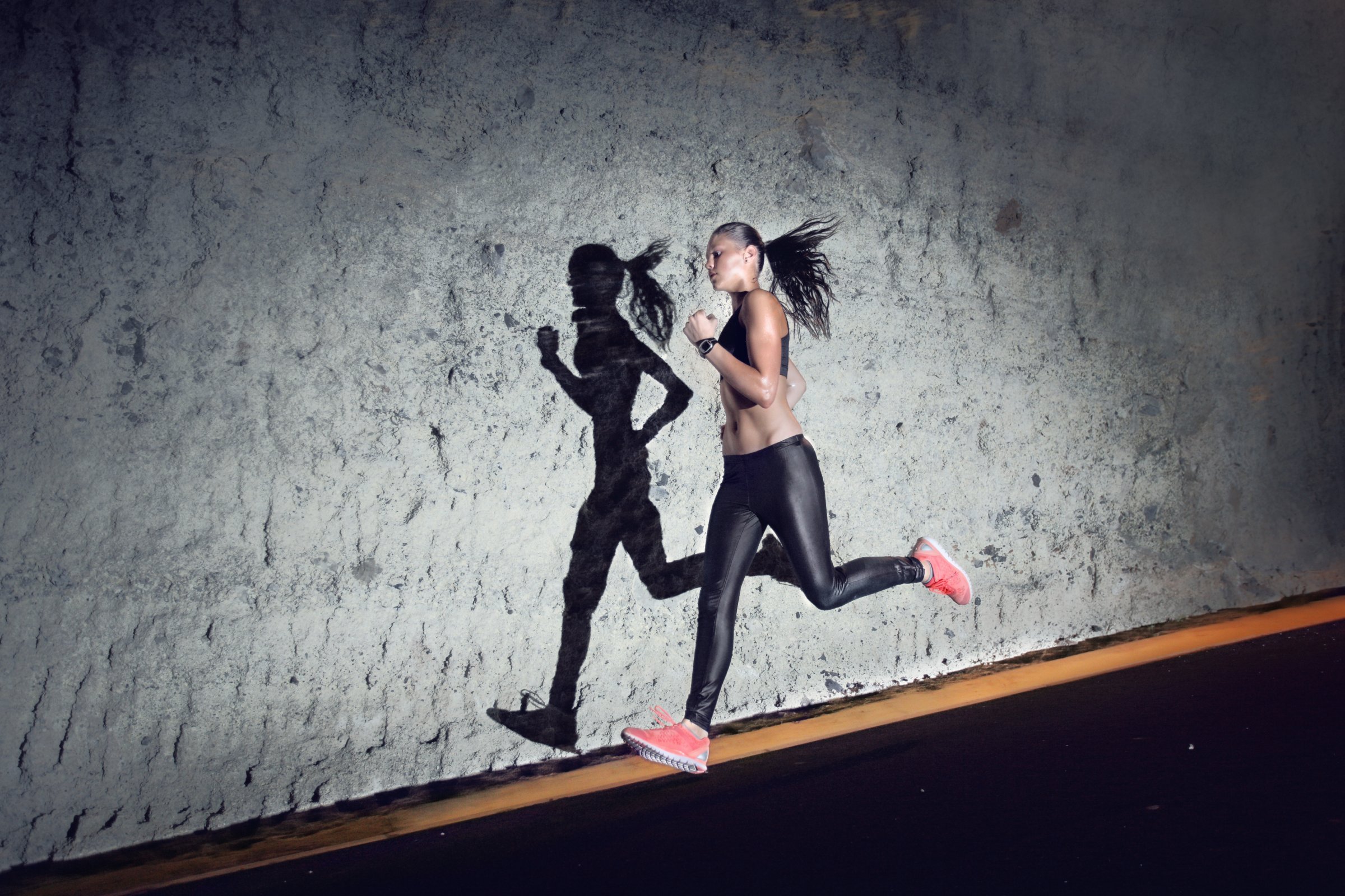 Woman running at night against grey wall